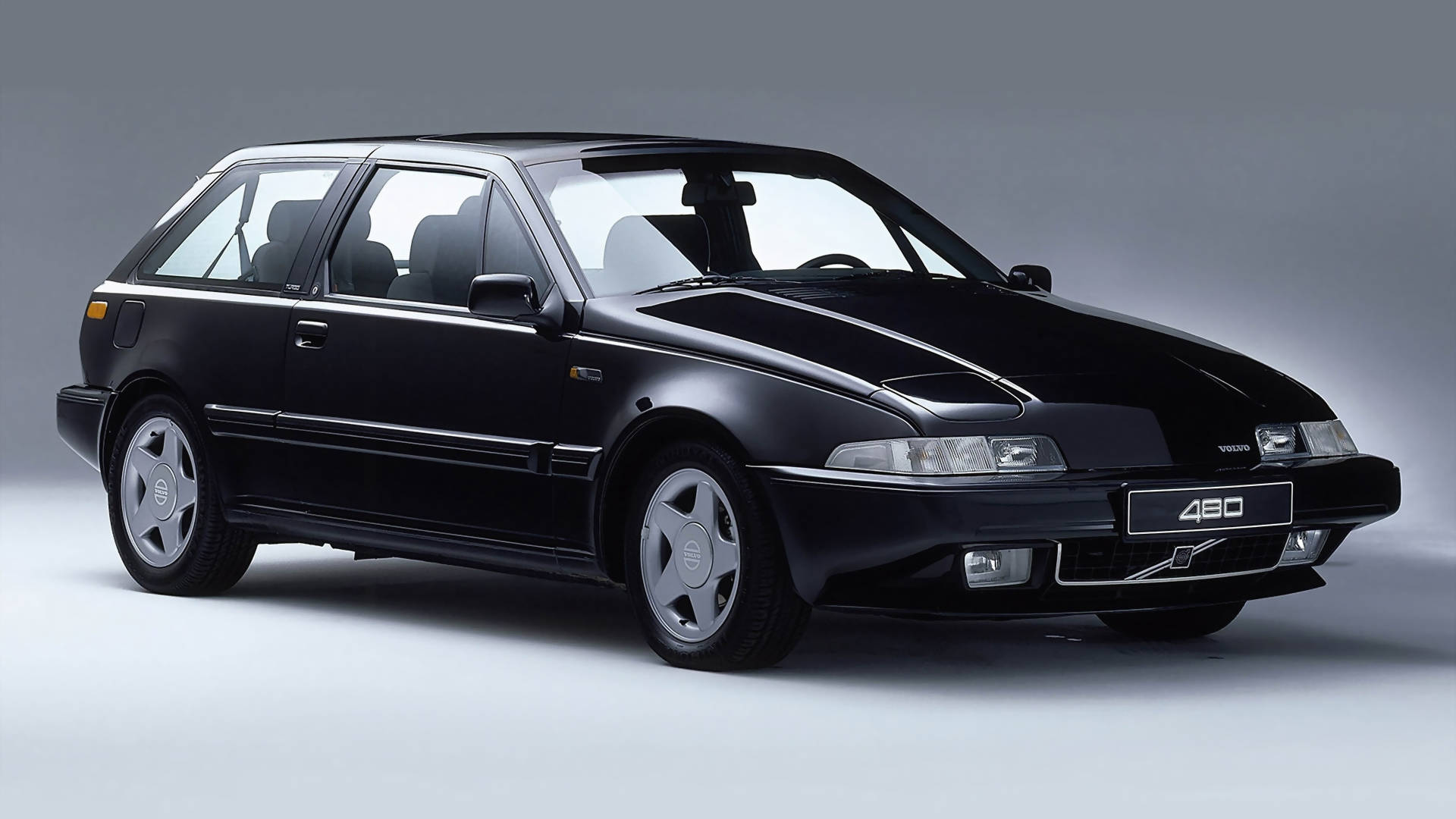 volvo iPhone 桌布 壁紙 — 一輛時尚的黑色富豪480掀背車在攝影棚燈光下，於簡約灰色背景前閃閃發光。