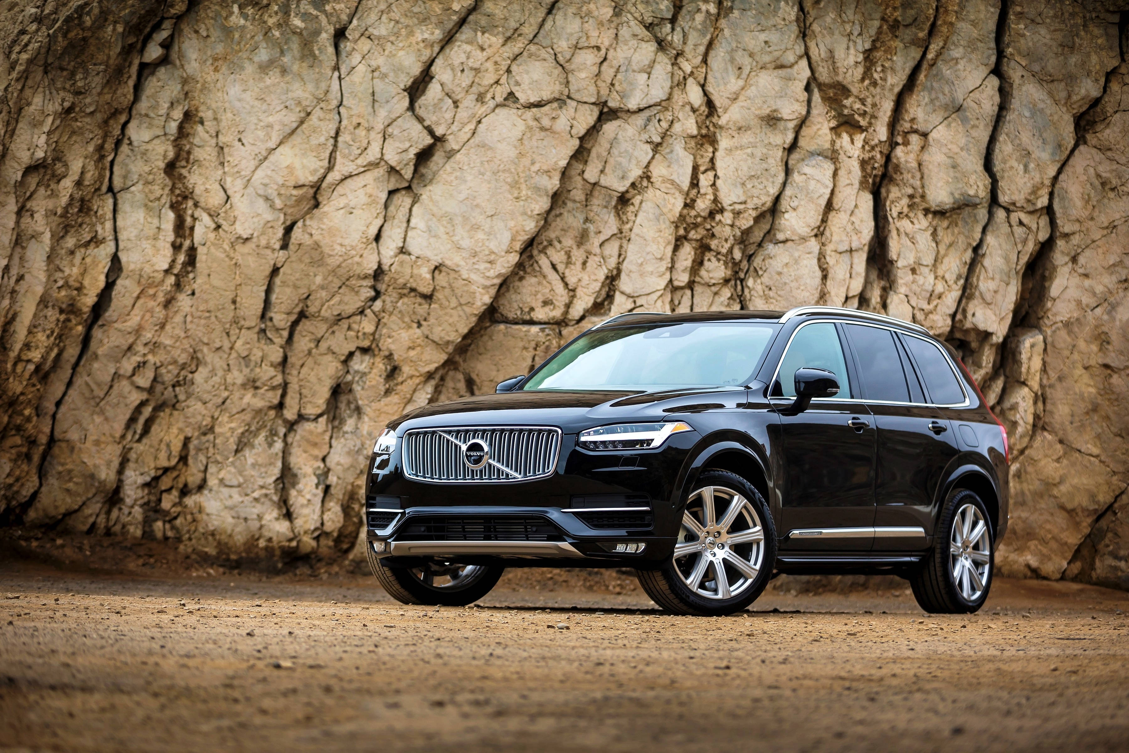 Volvo 桌布 壁紙 — 一輛時尚的黑色富豪XC90 SUV停放在泥土上，前方是粗糙紋理的岩石峭壁。