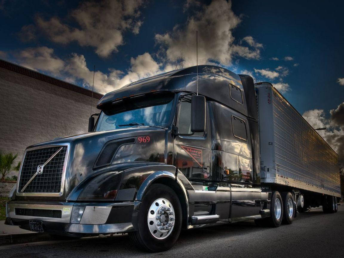 Trucks 桌布 壁紙 — 一輛時尚的黑色富豪半掛卡車帶有鍍鉻裝飾，停在瀝青場地上，反射出戲劇性的多雲天空。