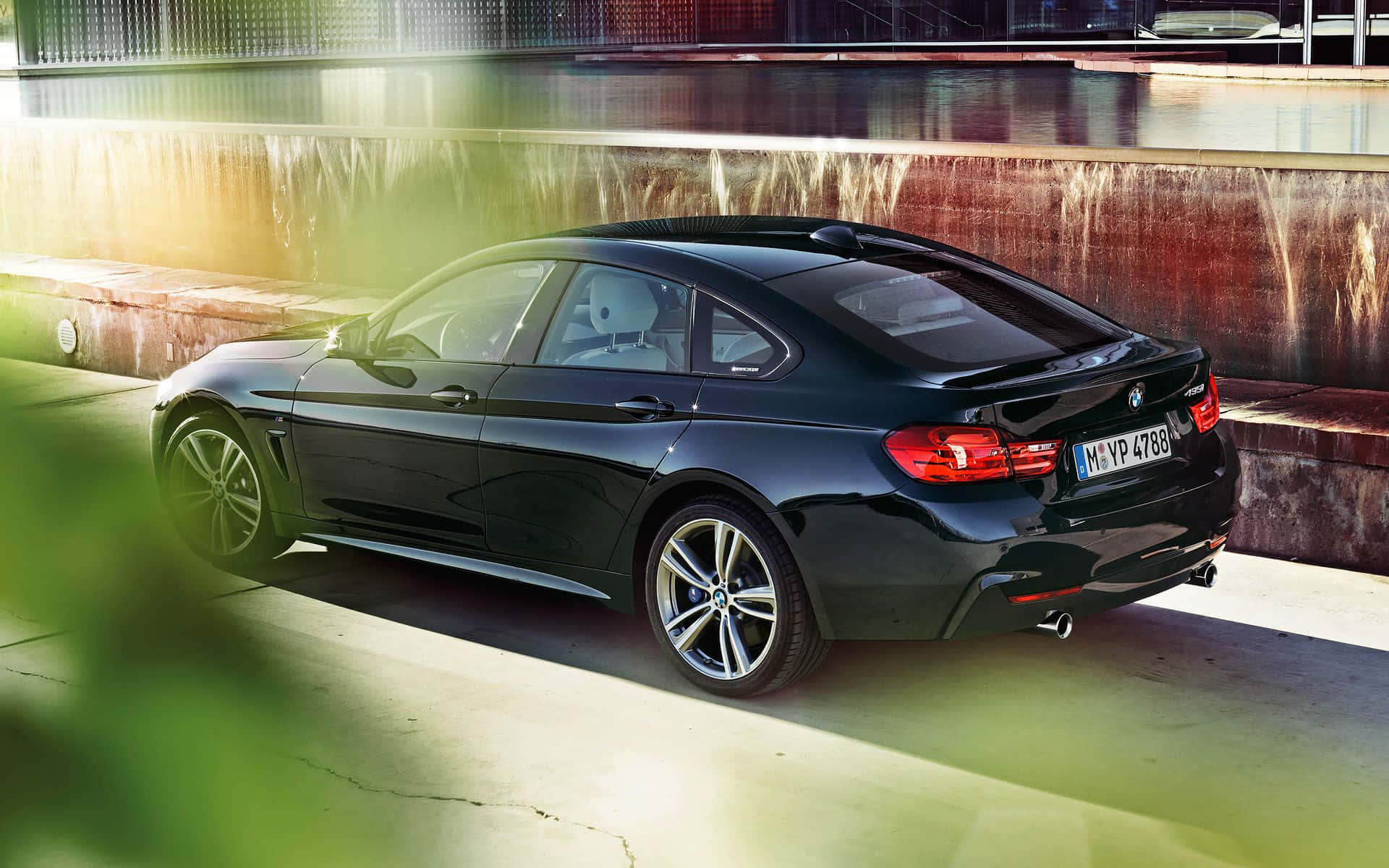 Bmw 4 Series 桌布 壁紙 — 一輛時尚的黑色寶馬轎車停在水景旁邊，陽光穿過綠植灑落。