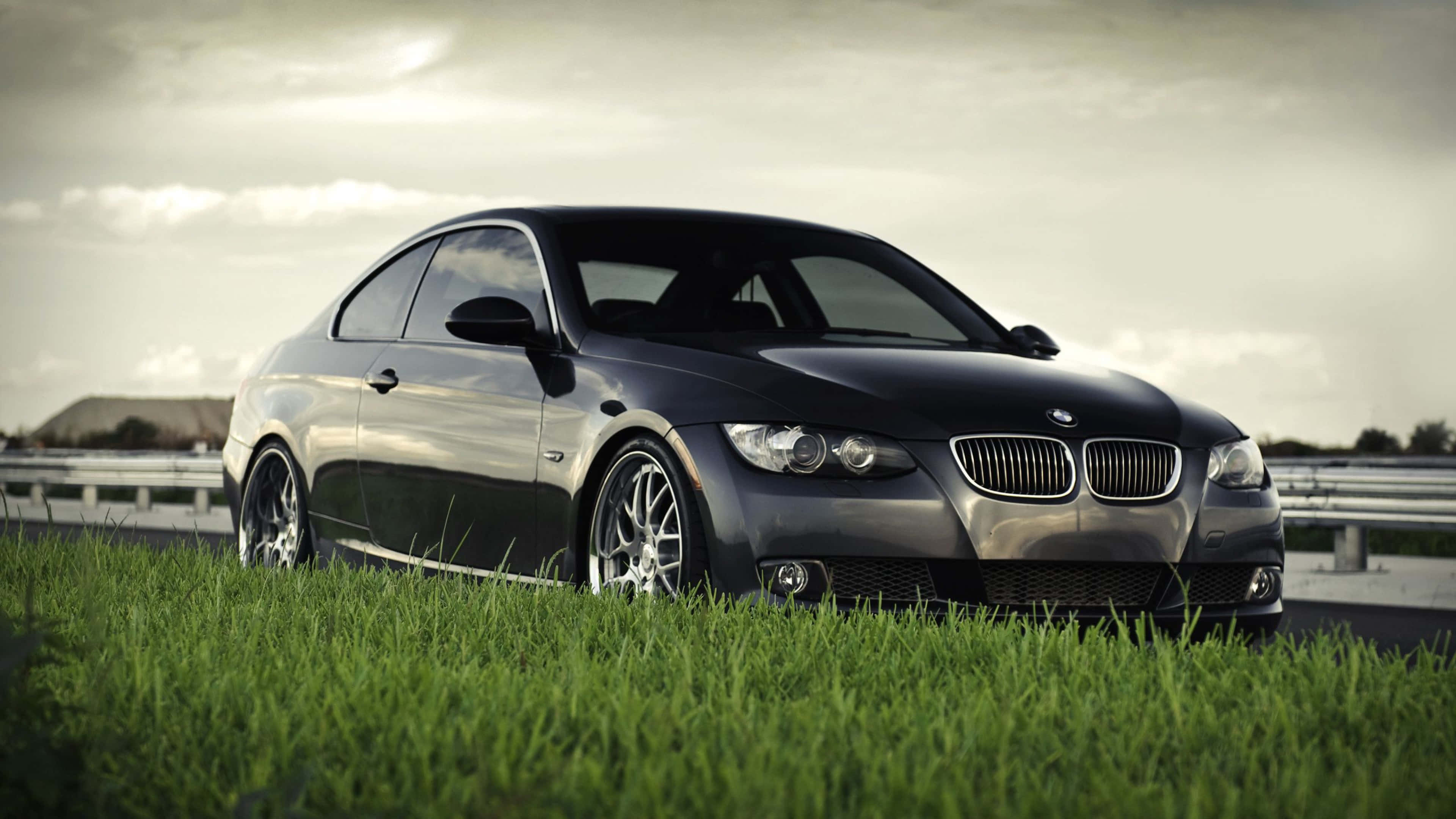 Bmw 328 桌布 壁紙 — 一輛時尚的黑色寶馬雙門轎跑車停在高速公路旁的草地上，天空多雲。