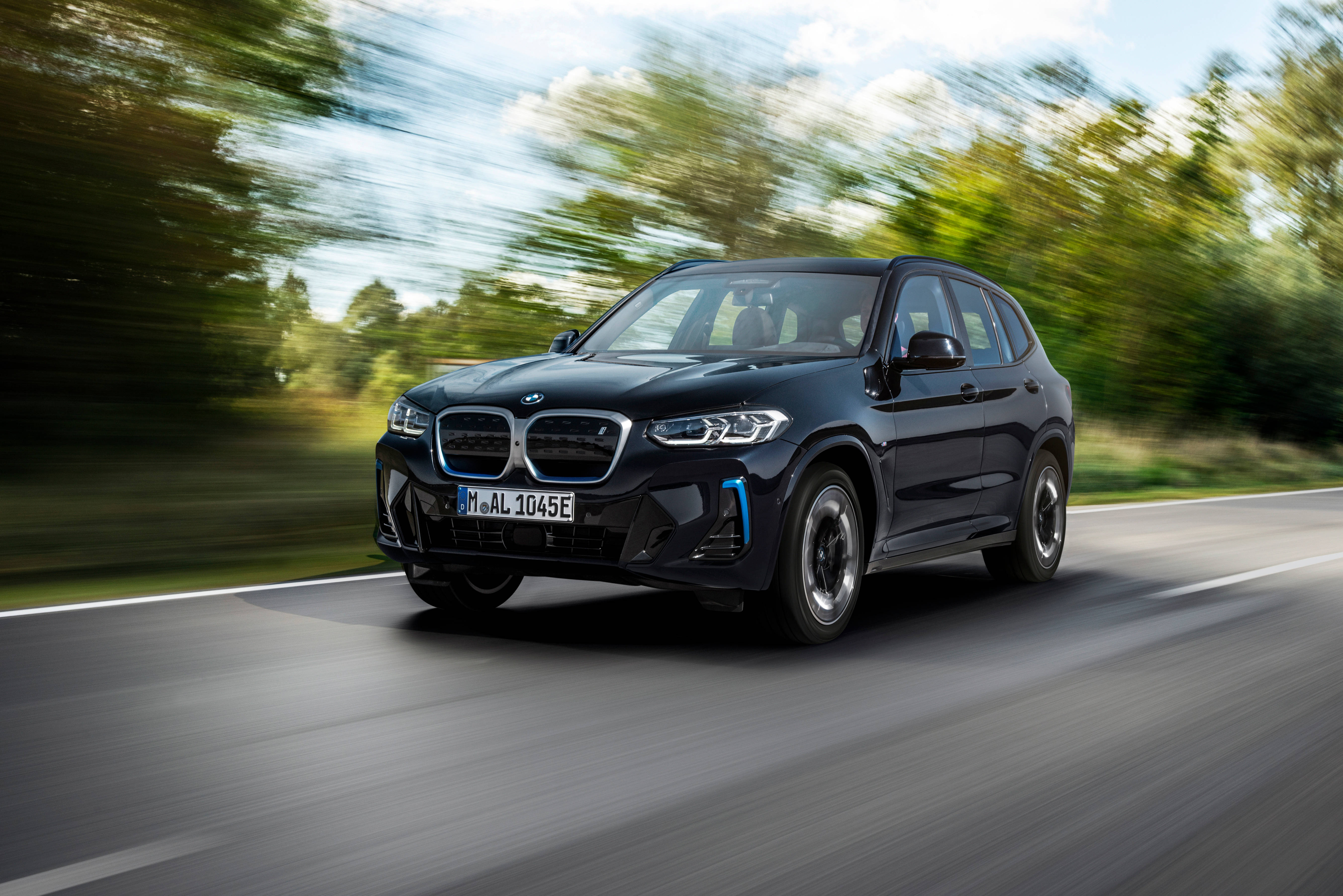 Black Bmw 桌布 壁紙 — 一輛時尚的黑色寶馬電動SUV在陽光明媚的道路上飛馳，模糊的綠色樹木從旁掠過。