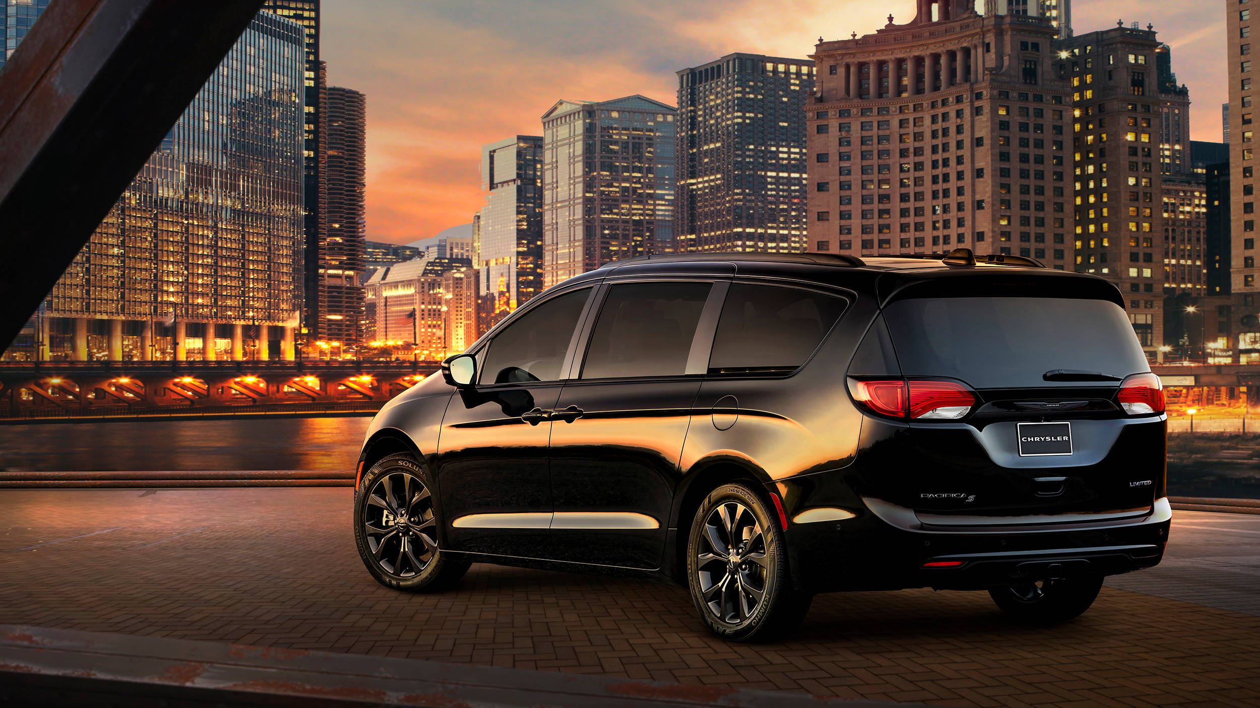 Chrysler 桌布 壁紙 — 一輛時尚的黑色小型貨車停泊在橋上，夕陽西下，背後是閃爍的城市天際線。