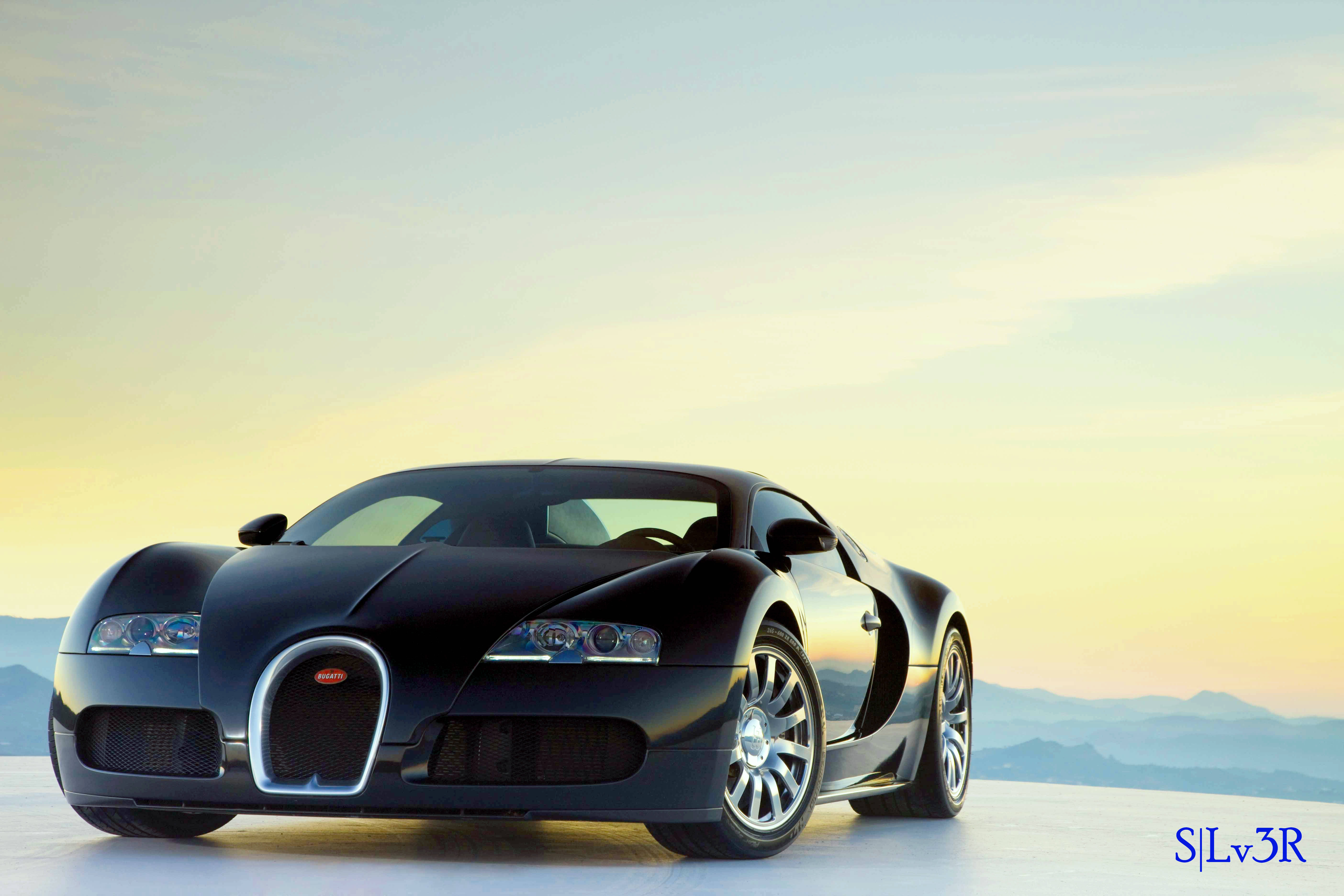bugatti iPhone 桌布 壁紙 — 一輛時尚的黑色布加迪超級跑車在金色日落光芒下閃耀，背景是遠處的山巒輪廓。