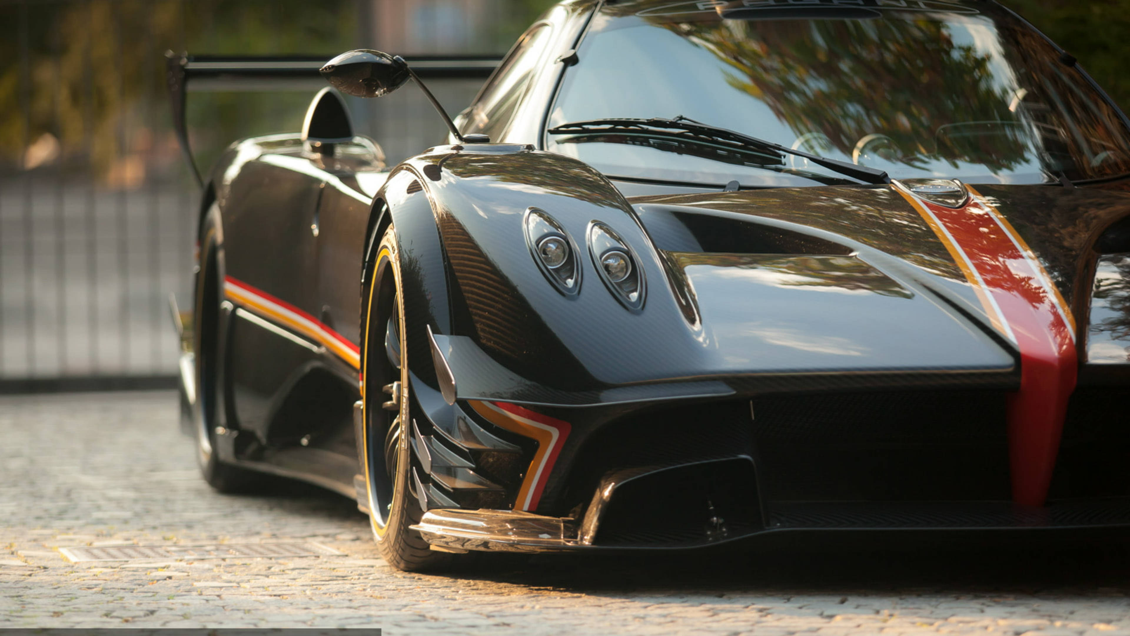 Pagani 桌布 壁紙 — 一輛時尚的黑色帕加尼Huayra跑車，帶有紅色和金色點綴，停在黃金時段的鵝卵石街道上。