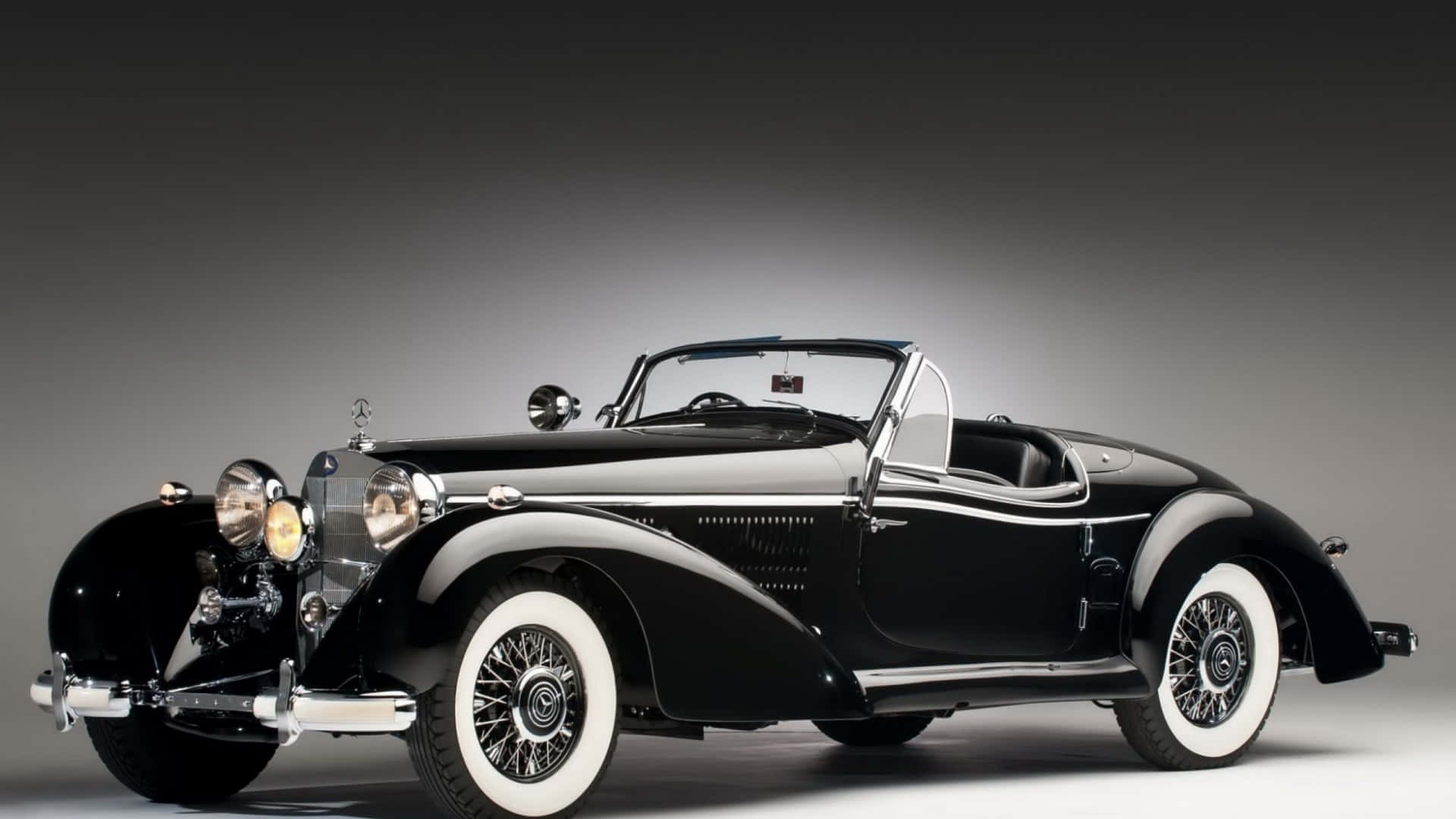 Vintage Car 桌布 壁紙 — 一輛時尚的黑色復古敞篷車，配備白邊輪胎和鍍鉻裝飾，在攝影棚燈光下閃閃發光。