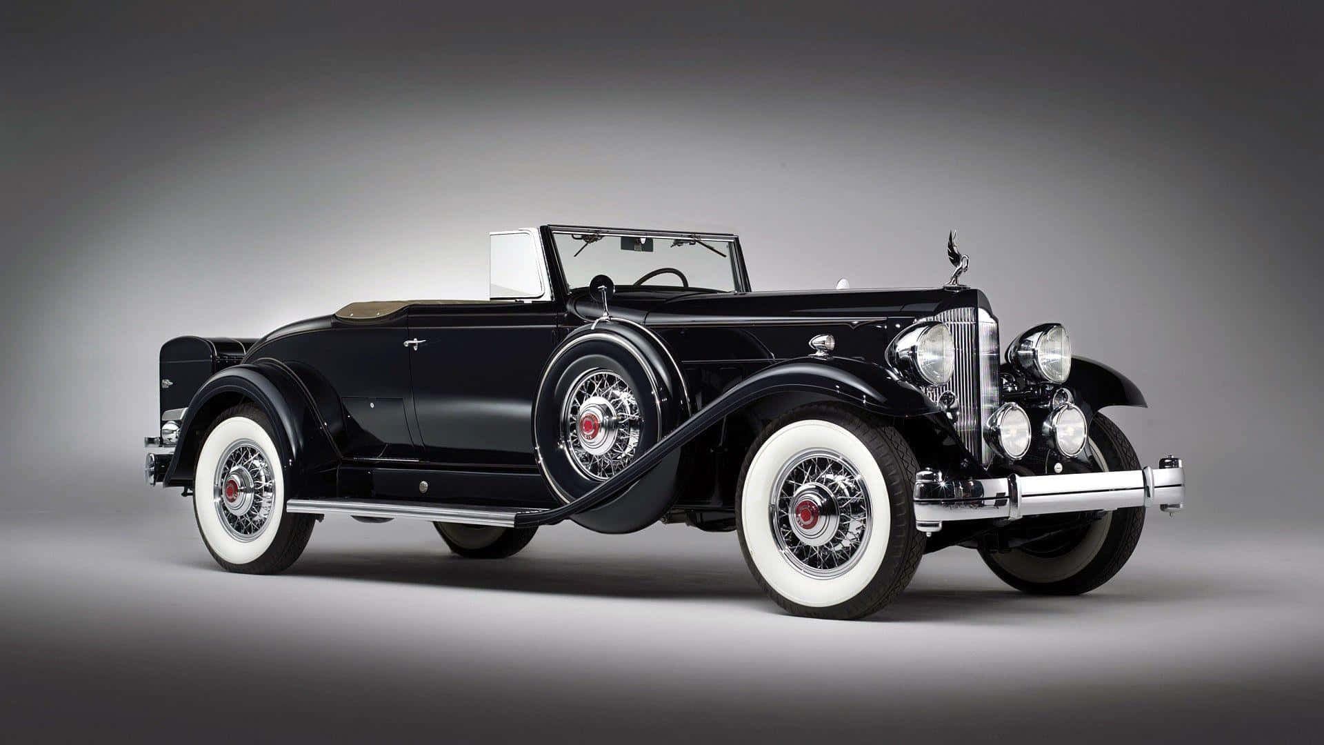 Black And White Vintage Car 桌布 壁紙 — 一輛時尚的黑色復古敞篷車，配備白邊輪胎和鍍鉻裝飾，在攝影棚燈光下閃閃發光。