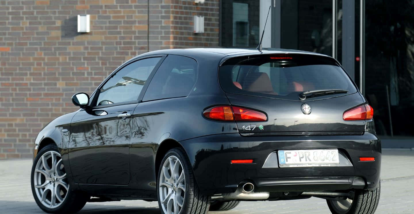 Alfa Romeo 147 桌布 壁紙 — 一輛時尚的黑色愛快羅密歐147跑車停放在戶外，背景是磚砌建築。