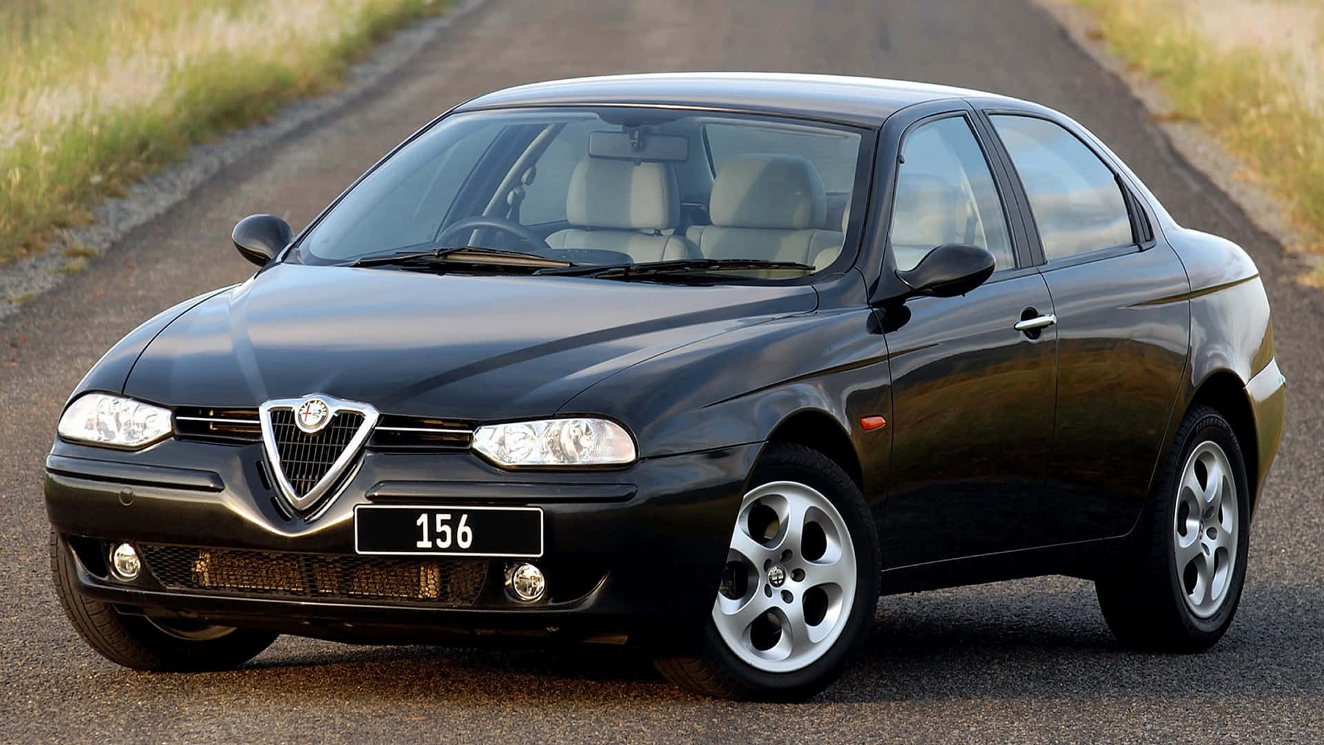 Alfa Romeo 156 桌布 壁紙 — 一輛時尚的黑色愛快羅密歐156轎車停泊在碎石路上，背景是草地田野。