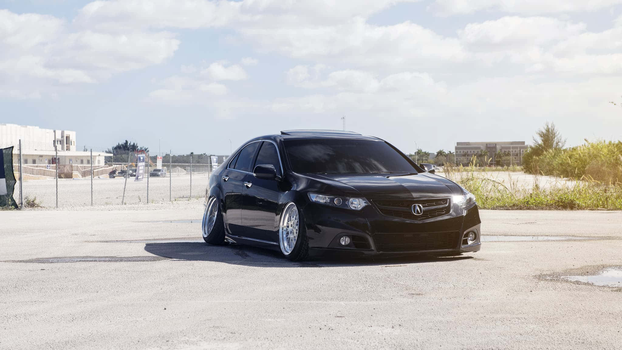 Acura Tsx 桌布 壁紙 — 一輛時尚的黑色改裝轎車配備定制輪圈，停在明亮的陰天下裂開的瀝青路面上。
