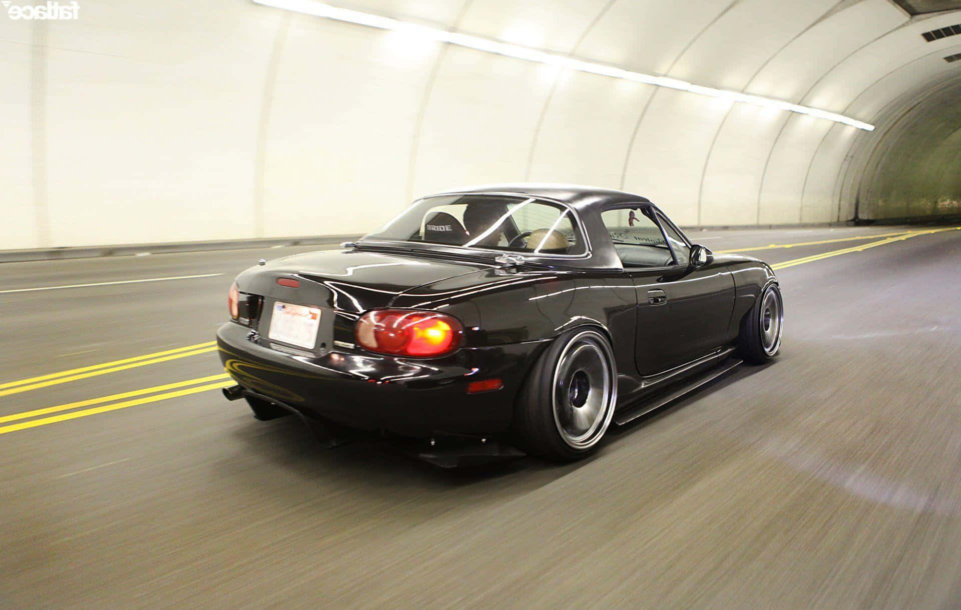 Miata 桌布 壁紙 — 一輛時尚的黑色敞篷跑車在燈光明亮的隧道中疾馳，道路上帶有動態模糊效果。