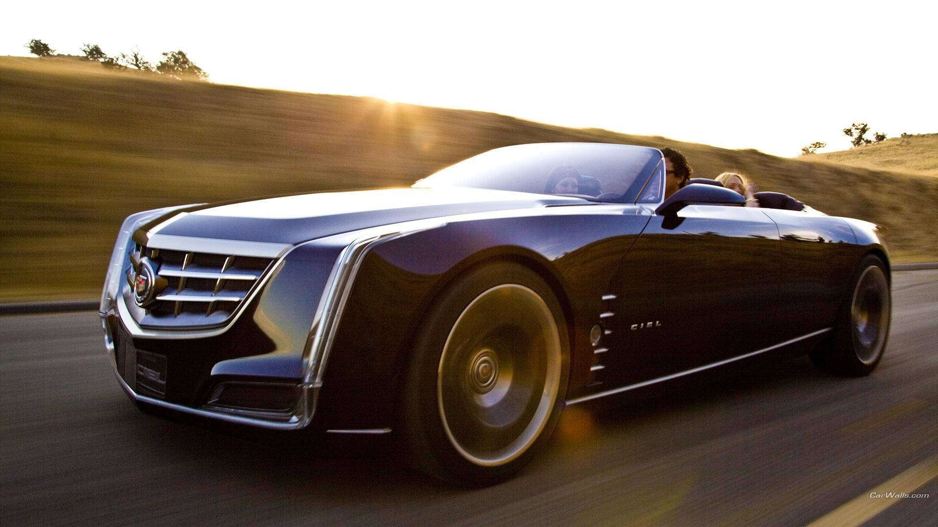 Cadillac 桌布 壁紙 — 一輛時尚的黑色敞篷跑車在陽光明媚的山路上疾馳，帶有模糊的動感和金色光線。