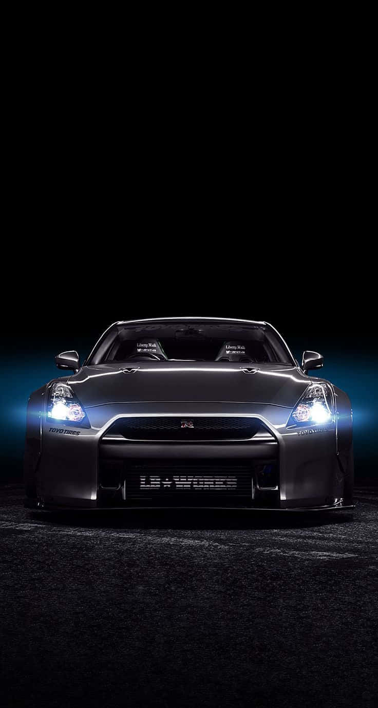 Nissan Skyline 桌布 壁紙 — 一輛時尚的黑色日產GT-R跑車，配備發光的車頭燈，在帶有藍色燈光點綴的黑暗背景下凝視前方。