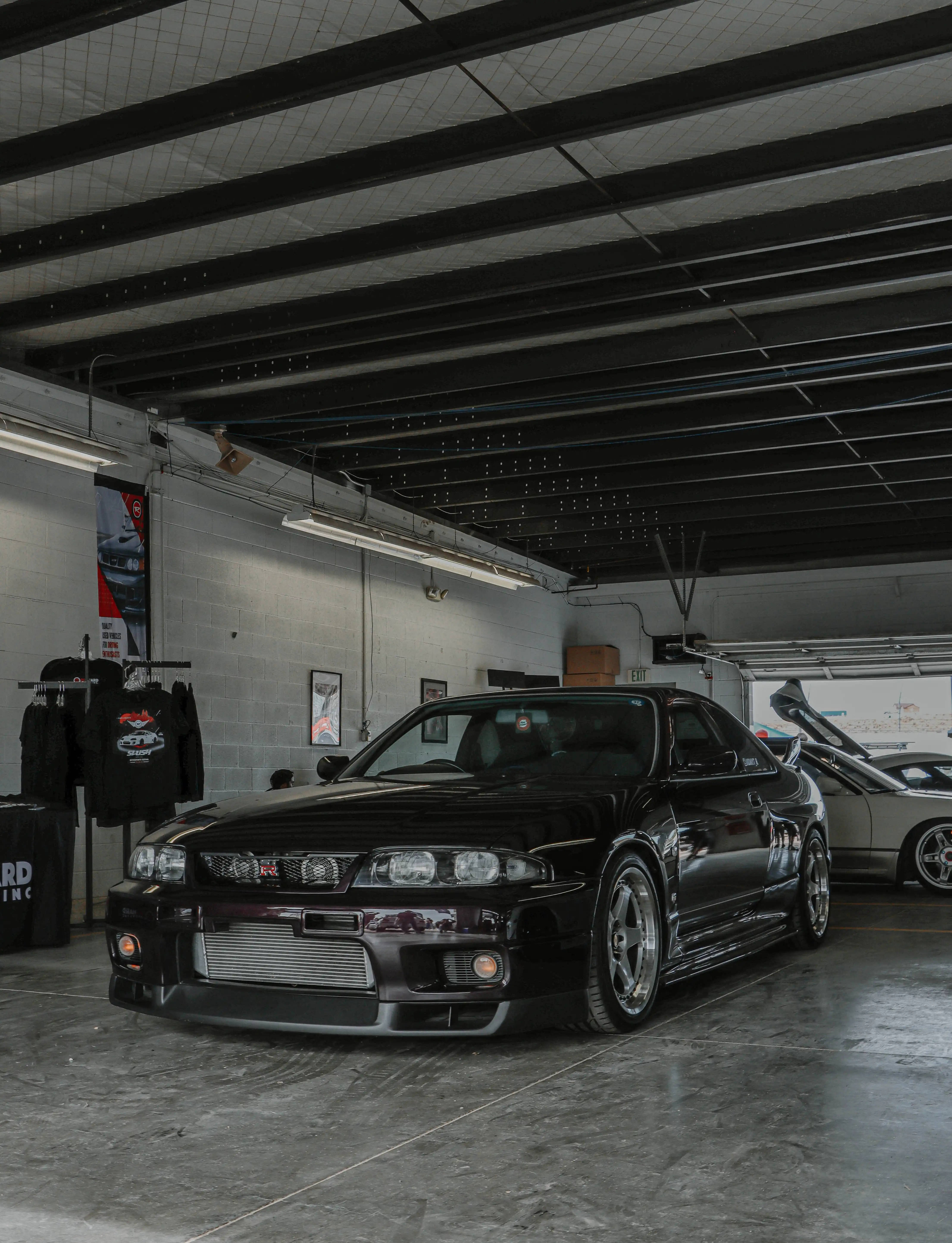 Nissan 桌布 壁紙 — 一輛時尚的黑色日產Skyline GT-R停放在高天花板、裸露橫樑和混凝土地板的車庫中。