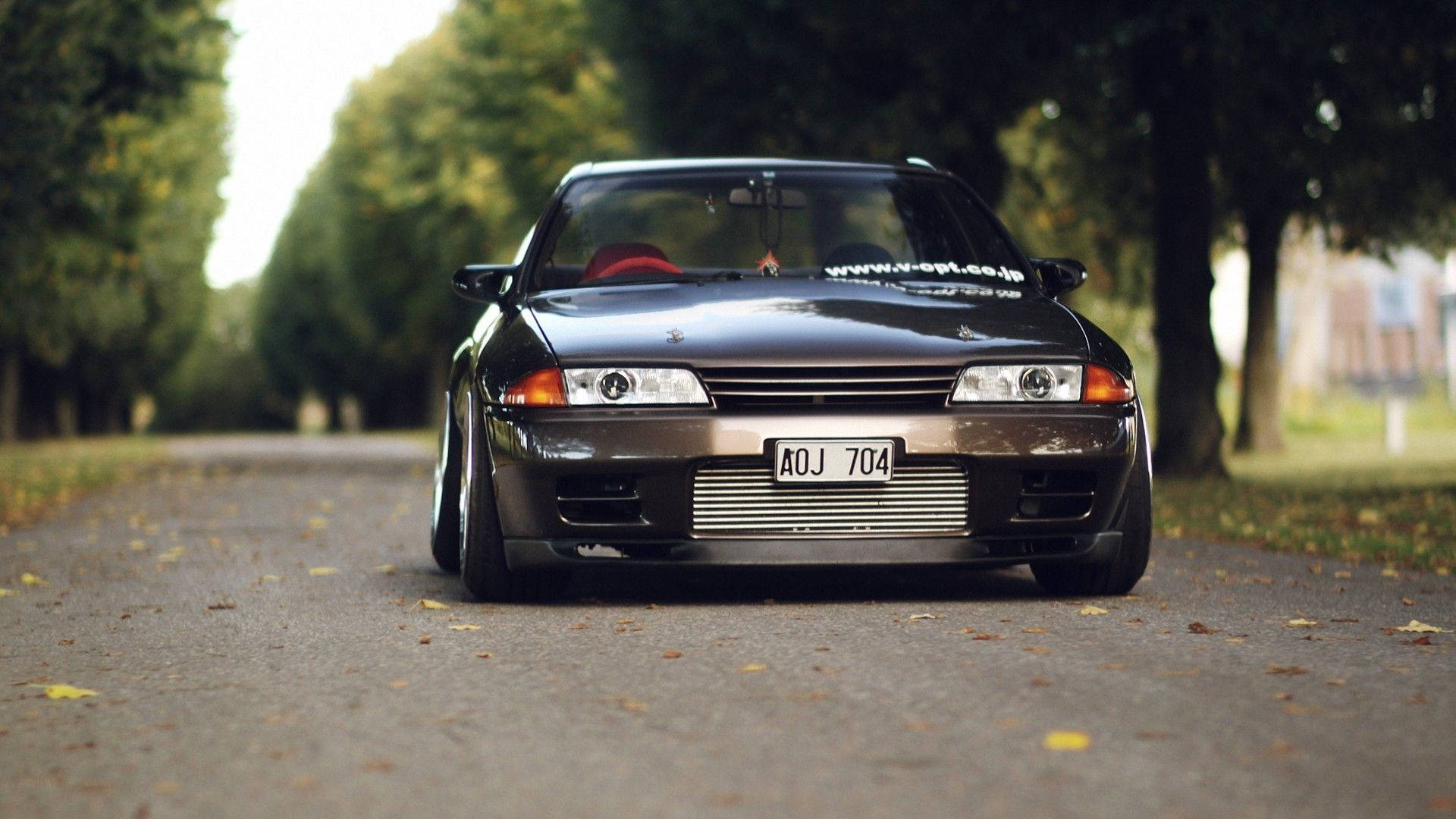 JDM 桌布 壁紙 — 一輛時尚的黑色日產Skyline GT-R在落葉滿地的秋日林蔭道上飄移。