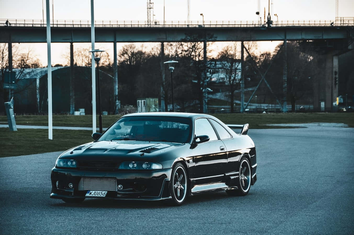 R33 GT-R 桌布 壁紙 — 一輛時尚的黑色日產Skyline GT-R在黃昏時停泊在橋下的瀝青路上，背景有光禿禿的樹木。