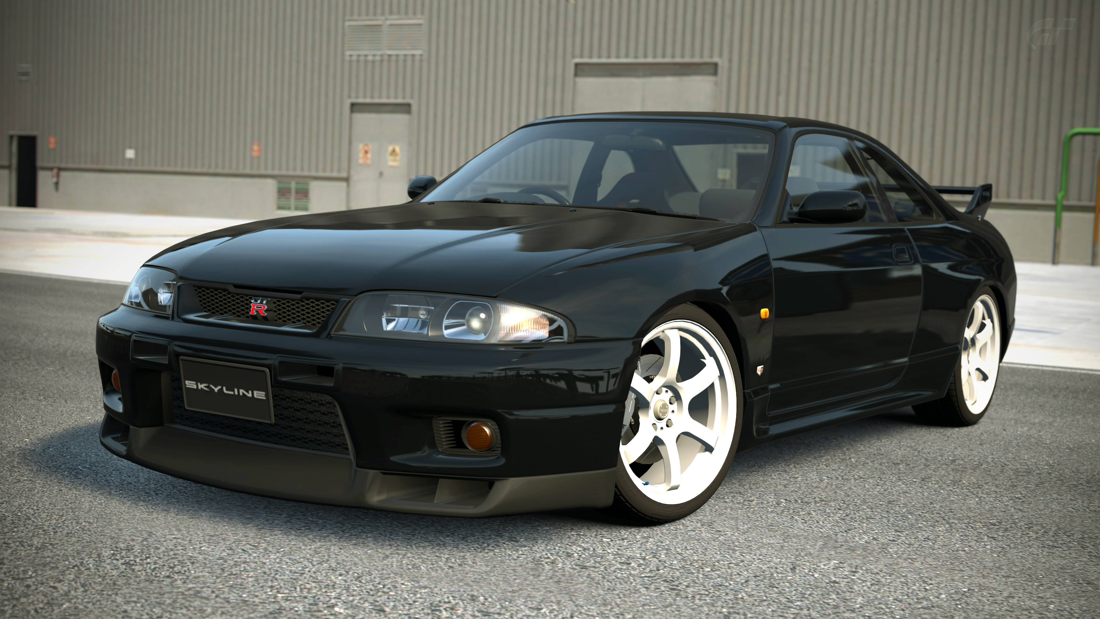 Gtr 桌布 壁紙 — 一輛時尚的黑色日產Skyline R34跑車搭配白色輪圈，停在灰色工業建築前的柏油路面上。