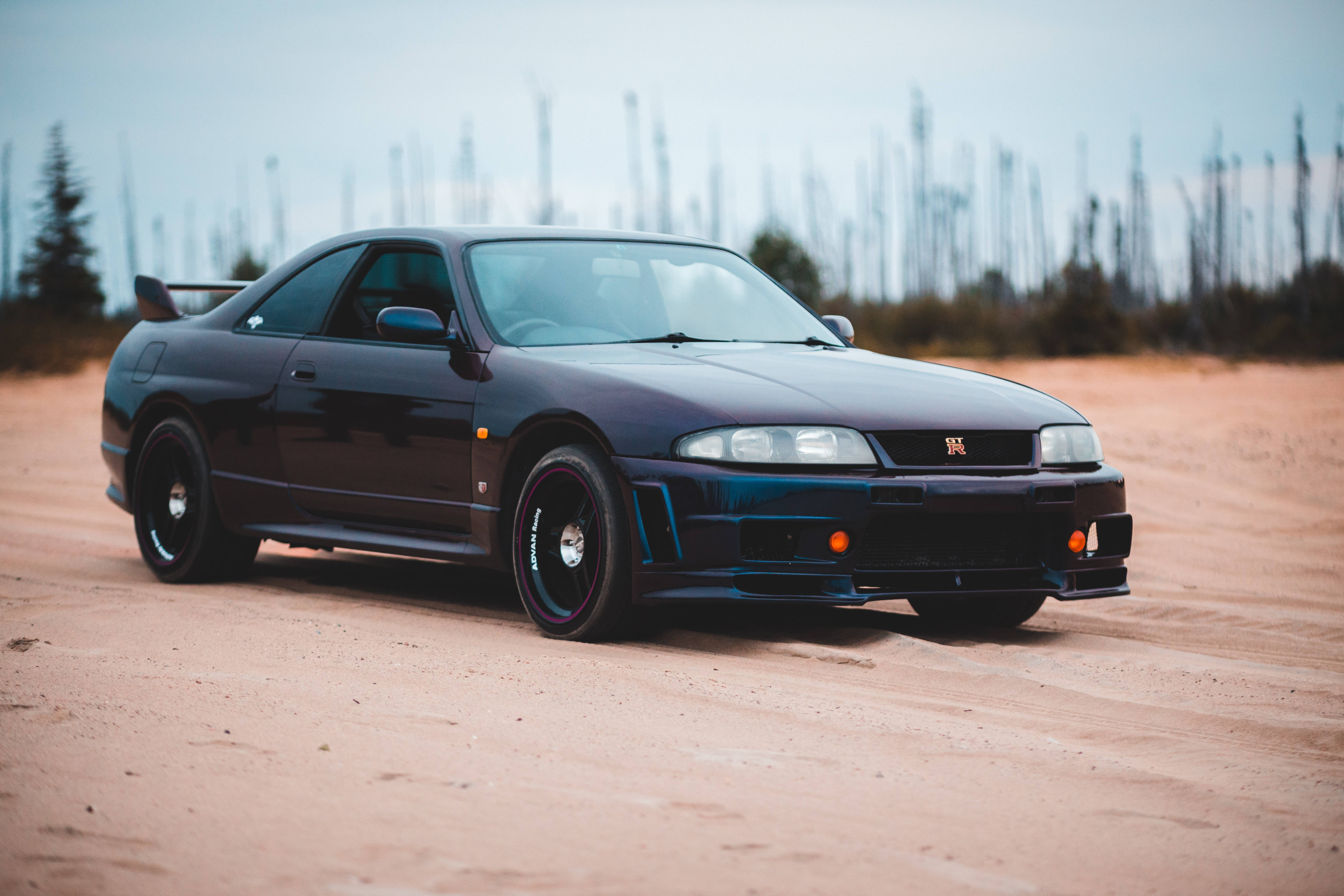 跑車 桌布 壁紙 — 一輛時尚的黑色日產Skyline R34跑車停放在塵土飛揚的越野地形上，背景有稀疏的樹木。