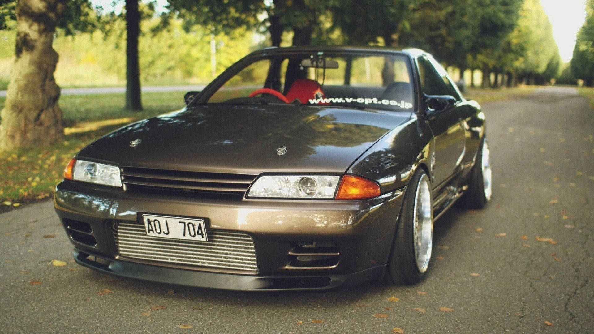 黑色日產Skyline R32跑車停在一條樹木成行的道路上，帶有秋葉。 — 4K Jdm 壁紙