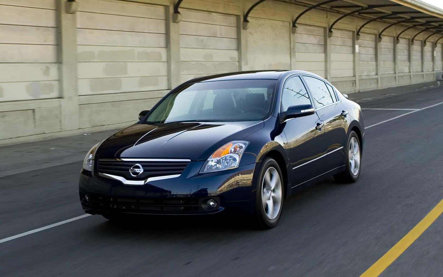 Nissan Altima 桌布 壁紙 — 一輛時尚的黑色日產轎車在陽光普照的高速公路上，在混凝土天橋下行駛，路面呈現動態模糊效果。