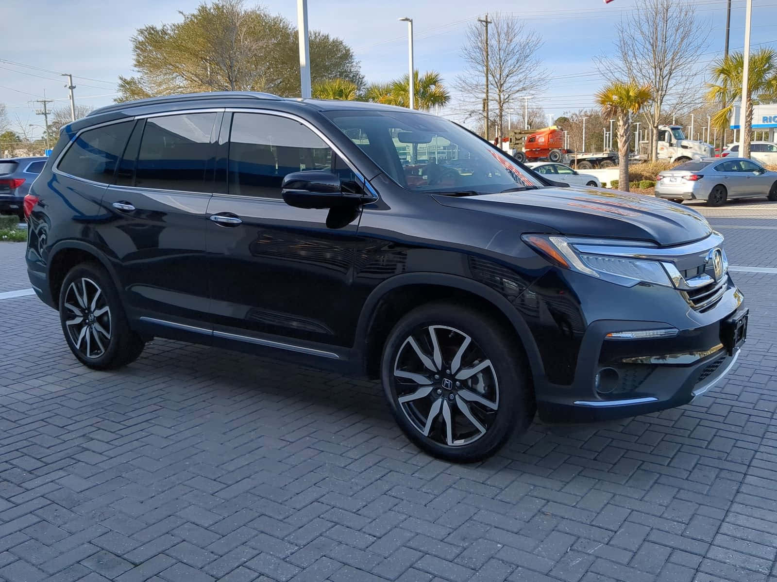 Honda Pilot 桌布 壁紙 — 一輛時尚的黑色本田Pilot SUV停放在灰色磚地上，背景是晴朗的藍天和棕櫚樹。