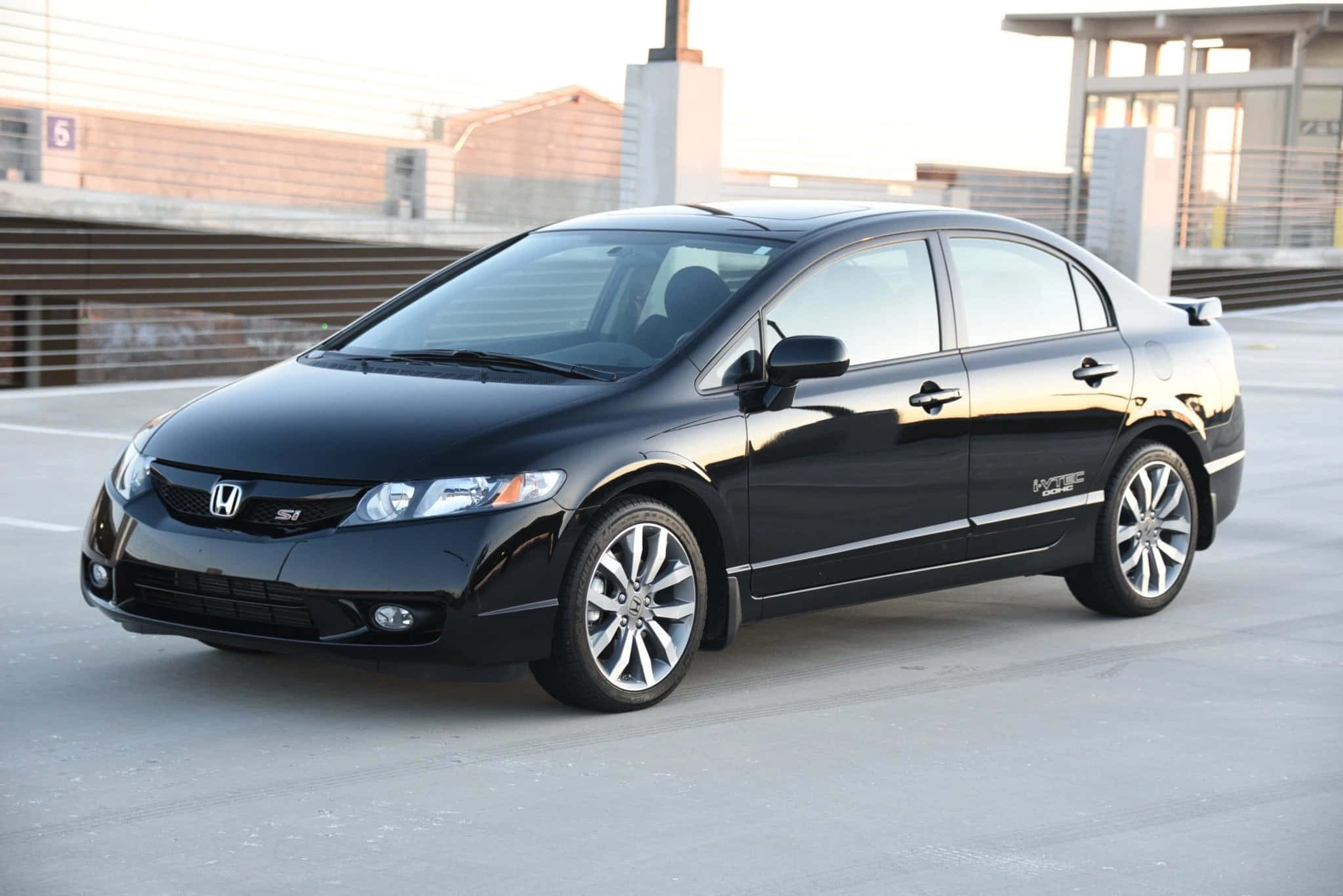 Honda Civic 桌布 壁紙 — 一輛時尚的黑色本田思域轎車在現代混凝土停車場的柔和日光下閃閃發光。
