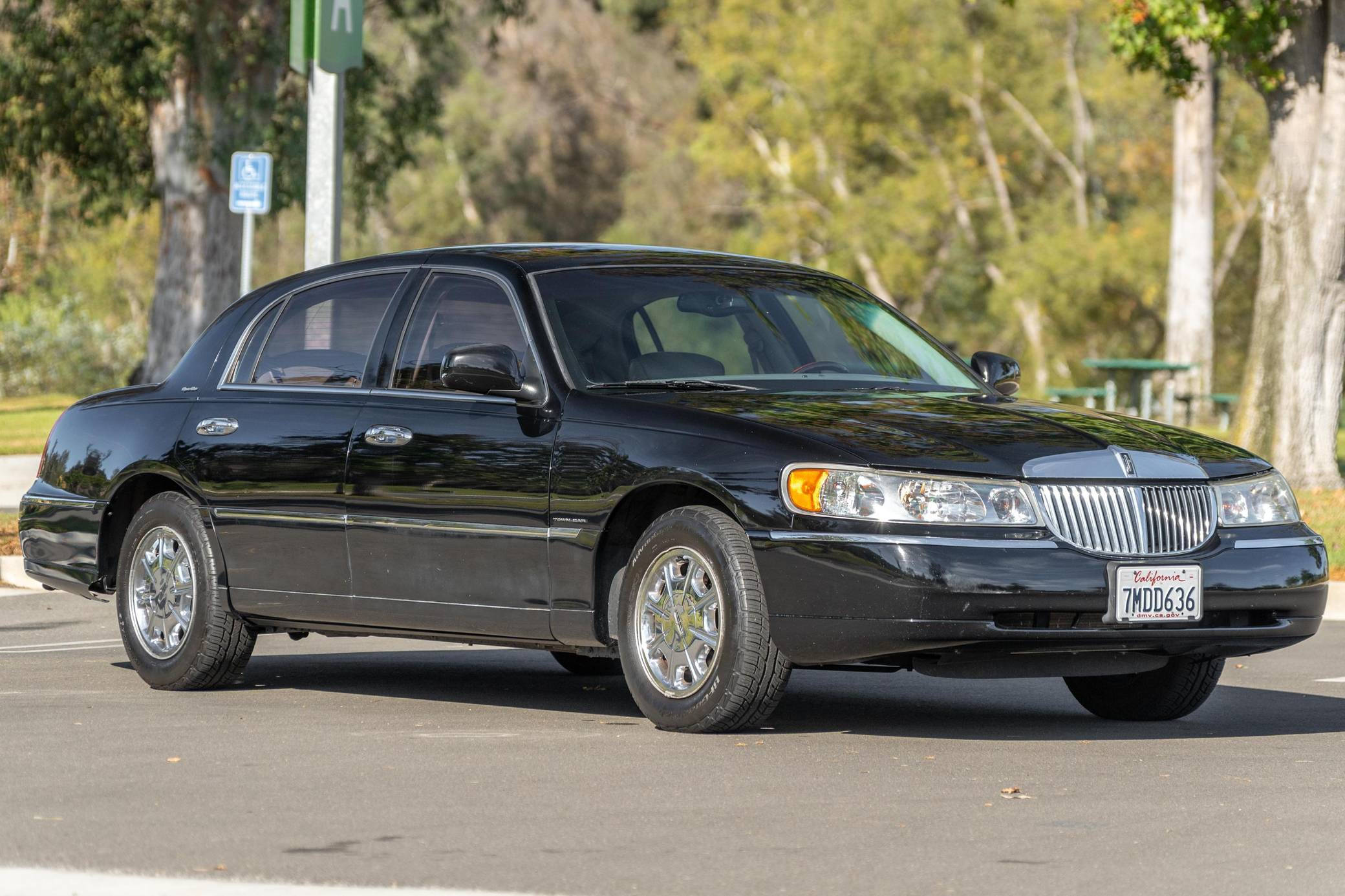 cars 桌布 壁紙 — 一輛時尚的黑色林肯Town Car停泊在陽光明媚的街道上，背景有樹木和野餐桌。
