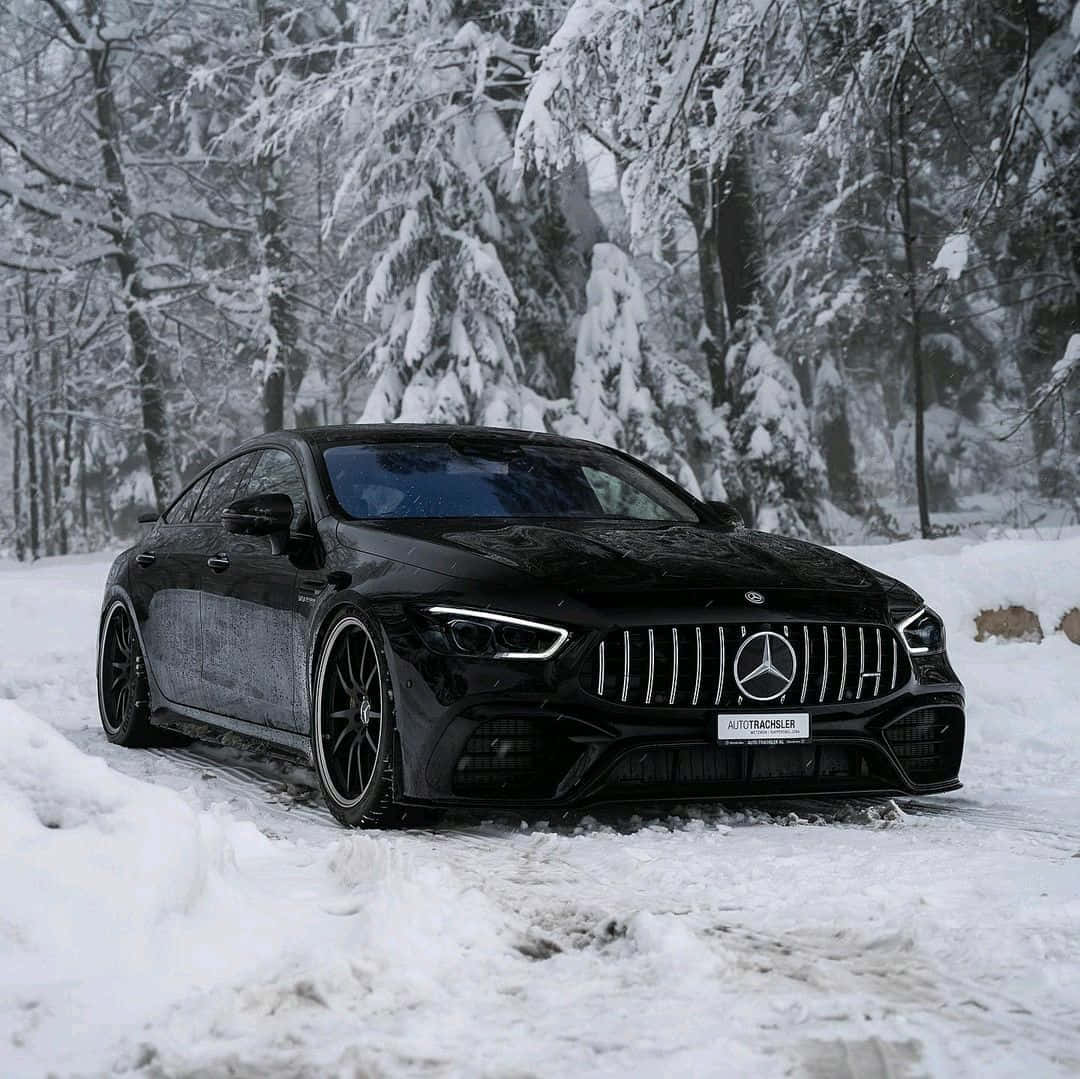 Winter Tires 桌布 壁紙 — 一輛時尚的黑色梅賽德斯-AMG GT停在雪覆蓋的森林中，周圍是積雪覆蓋的樹木和深厚的粉雪。