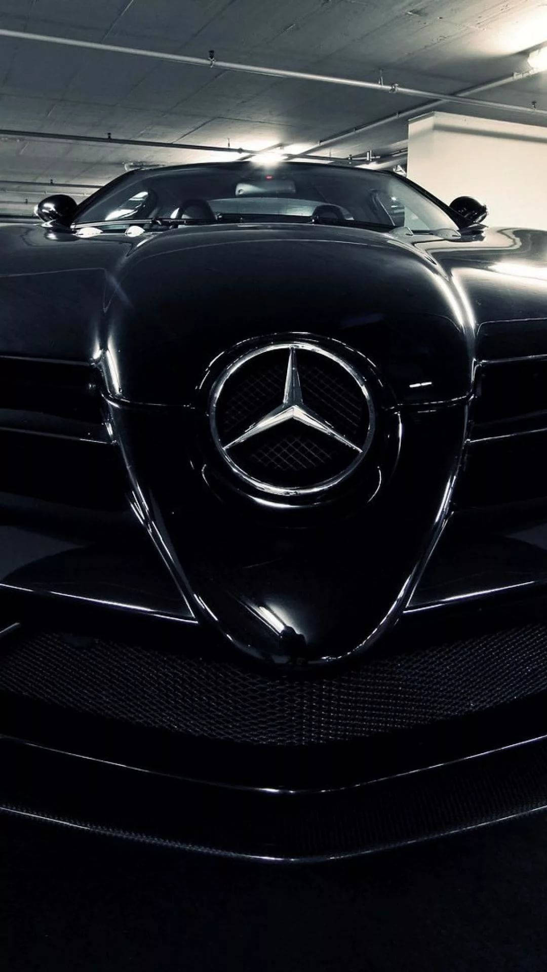 AMG iPhone 桌布 壁紙 — 一輛時尚的黑色梅賽德斯跑車在刺眼的車庫燈光下閃閃發光，配備碳纖維格柵和標誌性的星形徽章。