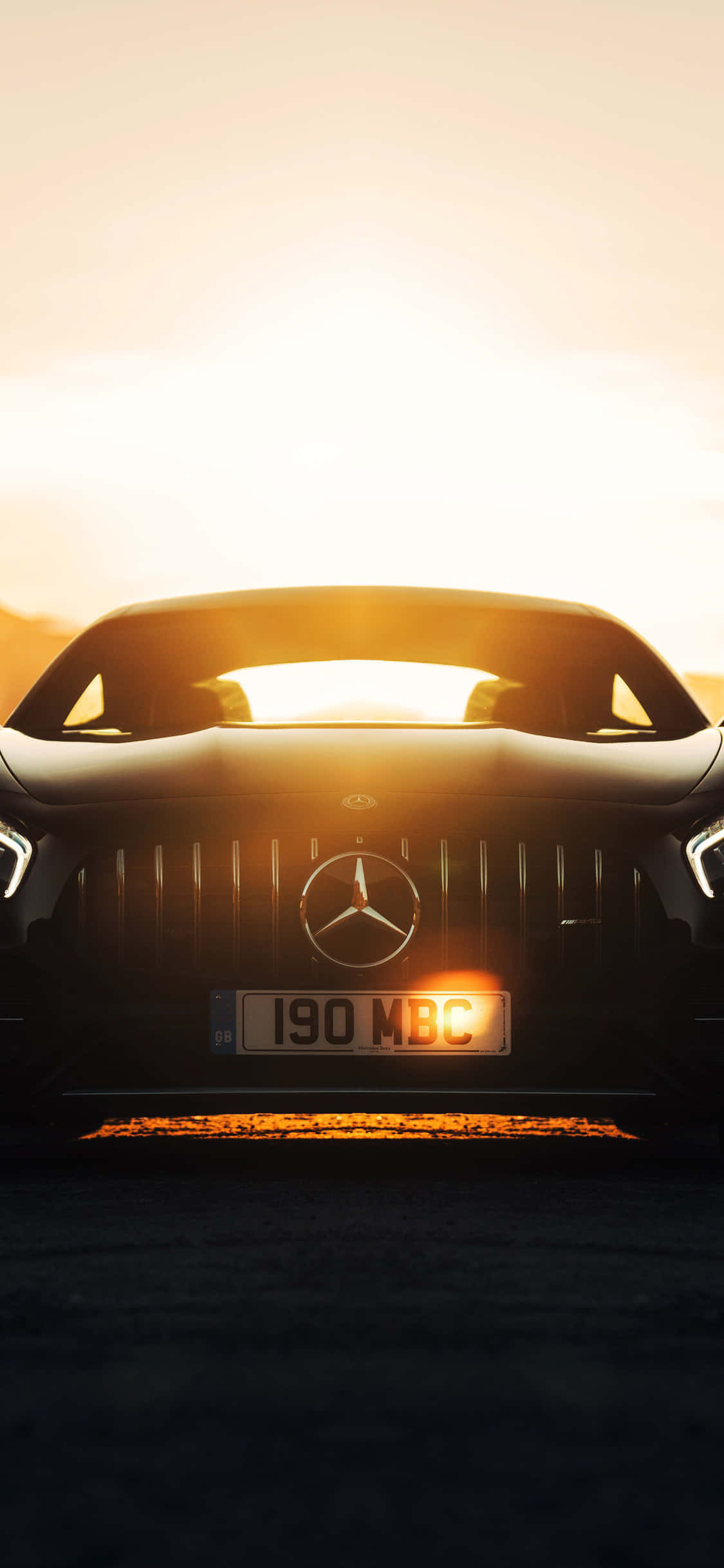 iPhone X Amg Gt-r 桌布 壁紙 — 一輛時尚的黑色梅賽德斯跑車面向鏡頭，金色夕陽的光芒在其水箱護罩和擋風玻璃後方閃耀。