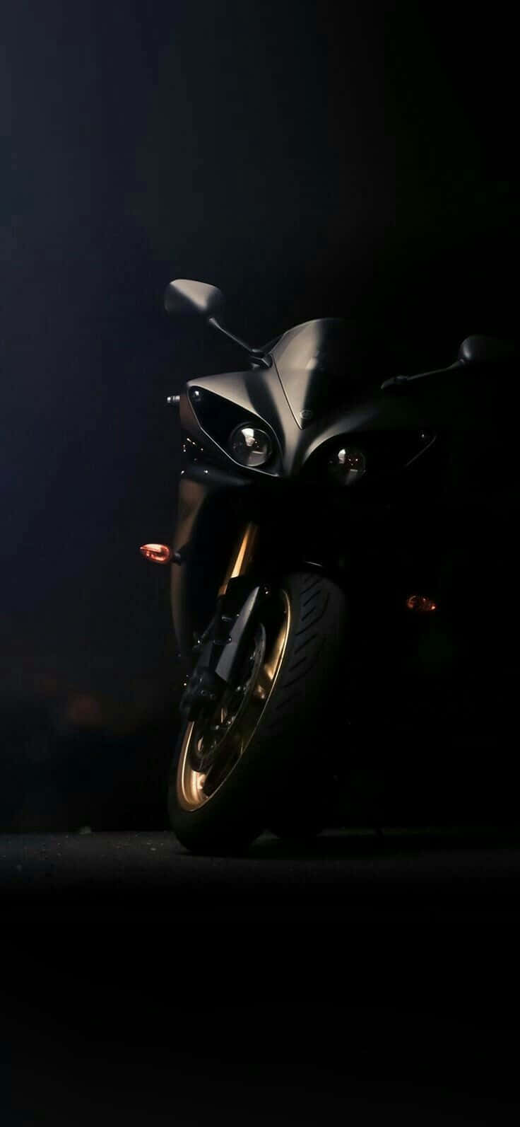 Superbike 桌布 壁紙 — 一輛時尚的黑色機車配金色輪圈，在黑暗背景下被戲劇性地照亮，突顯其銳利輪廓和發光的頭燈。
