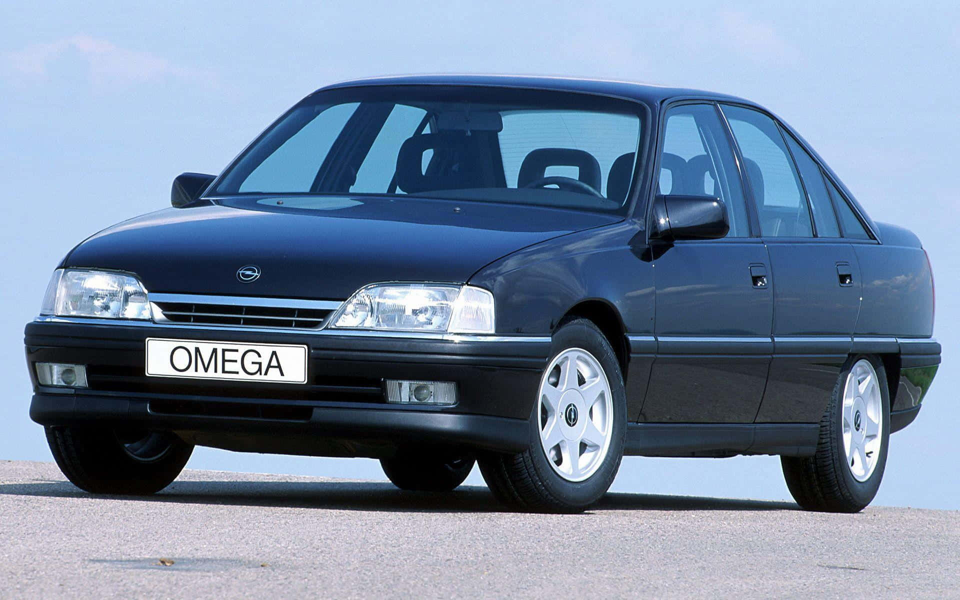 Opel Omega 桌布 壁紙 — 一輛時尚的黑色歐寶歐米茄轎車停在瀝青路面上，在清澈的藍天下，鍍鉻格柵和銀色合金輪圈閃閃發光。