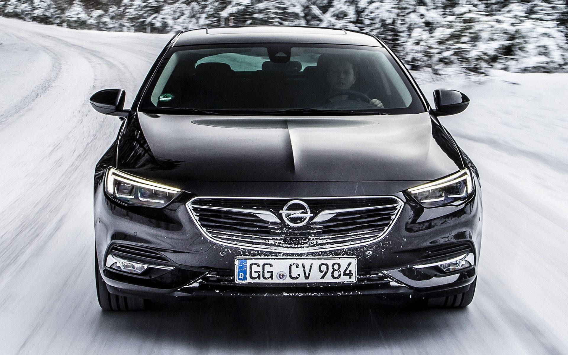 Opel 桌布 壁紙 — 一輛時尚的黑色歐寶轎車在積雪的森林道路上疾馳，動態模糊強調了其動態駕駛。