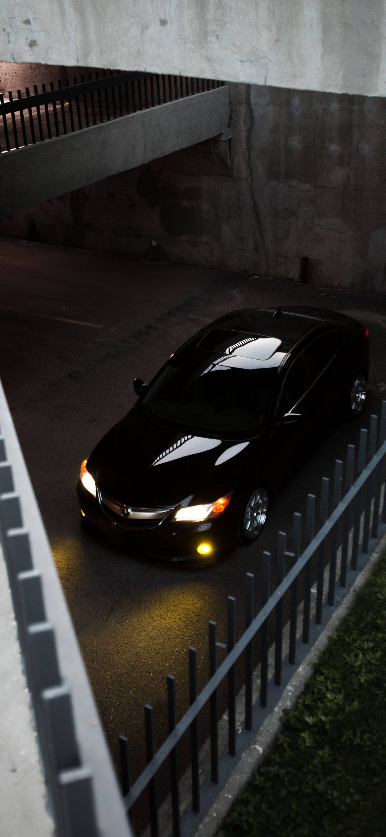 Cool Car 桌布 壁紙 — 一輛時尚的黑色汽車在夜間亮著車頭燈行駛在混凝土高架橋下。