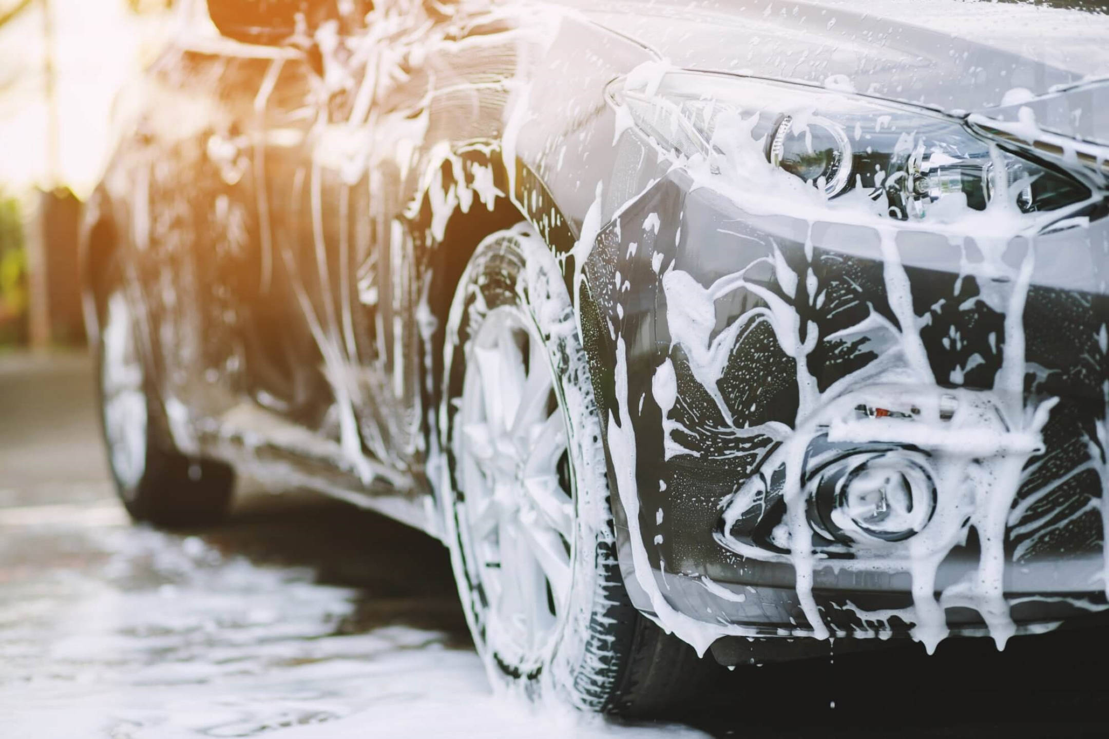 Wash 桌布 壁紙 — 一輛時尚的黑色汽車在溫暖的陽光下閃閃發光，濃厚的白色肥皂泡沫在徹底清洗期間沿著其閃亮表面傾瀉而下。
