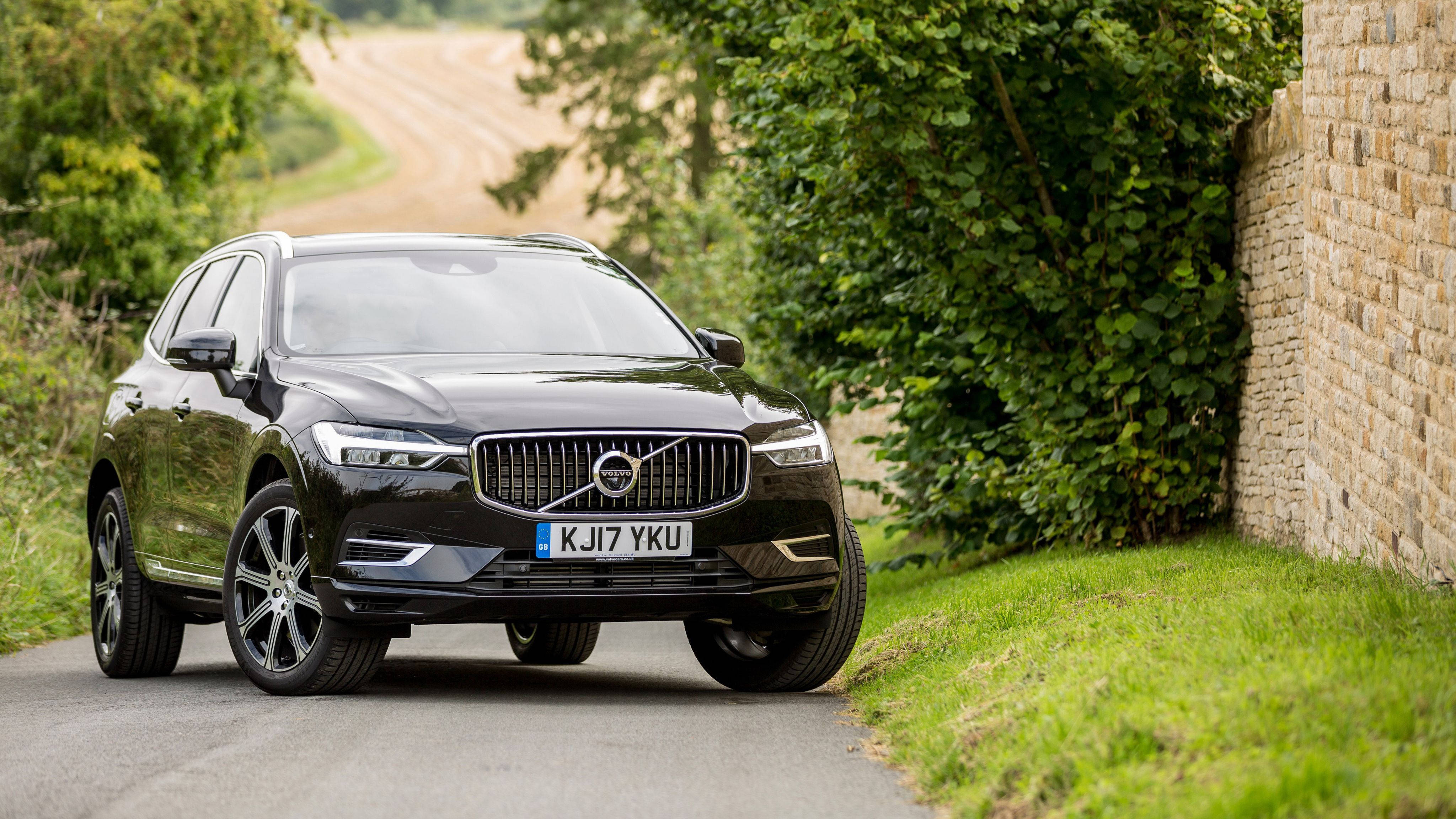Volvo 桌布 壁紙 — 一輛時尚的黑色沃爾沃XC60 SUV沿著蜿蜒的鄉村道路行駛，旁邊是石牆和茂密的綠植。