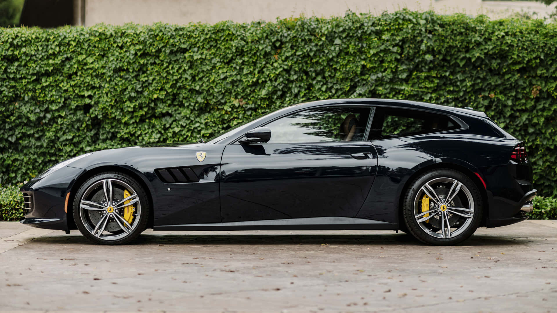 Ferrari Gtc4lusso 桌布 壁紙 — 一輛時尚的黑色法拉利 GTC4Lusso T 停在混凝土車道上，後面是茂密的綠色樹籬。