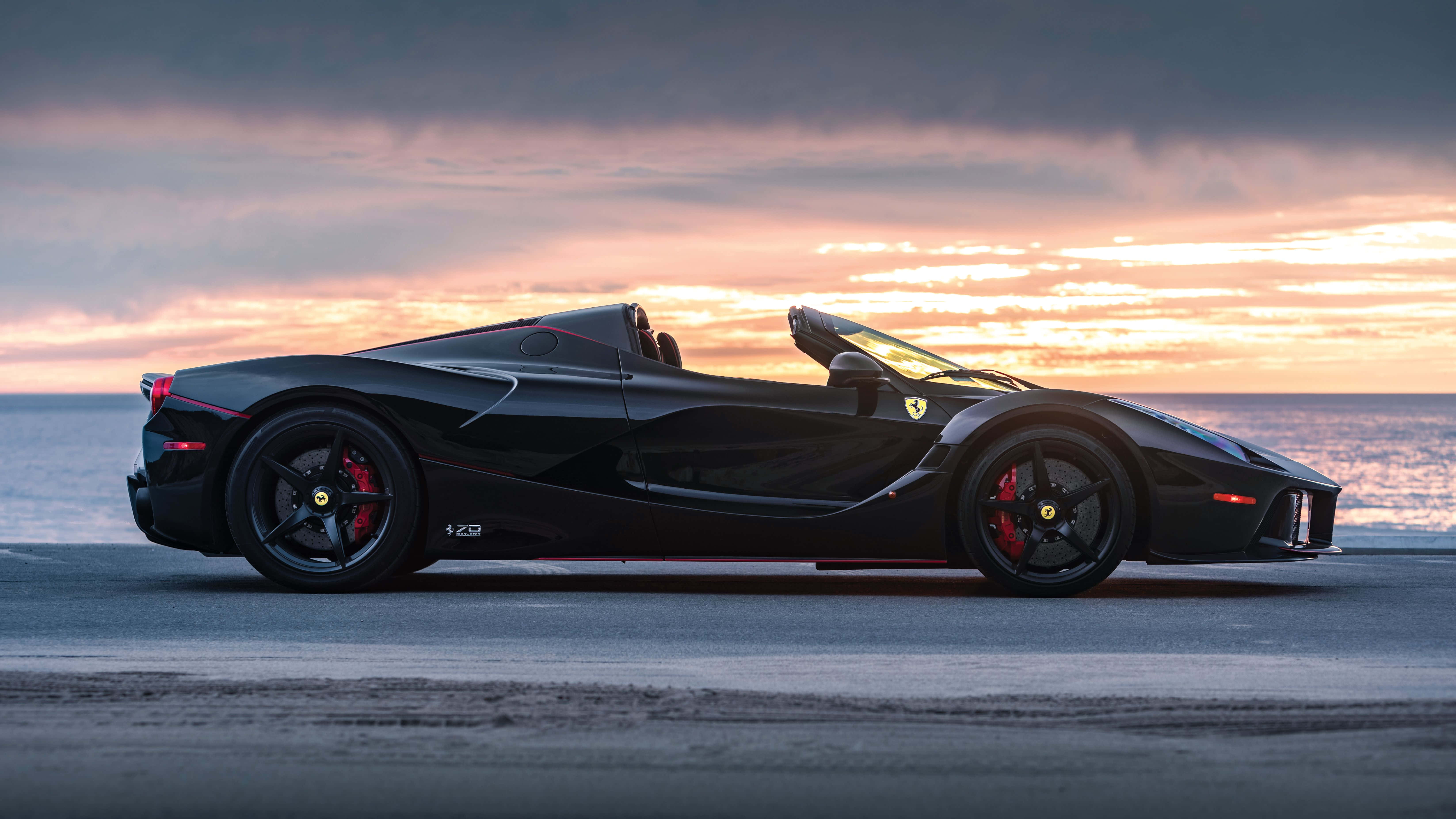Black Car 4K 桌布 壁紙 — 一輛時尚的黑色法拉利 LaFerrari Aperta 停泊在日落時分的海岸公路上，上空有鮮豔的橙色和粉紅色雲彩。