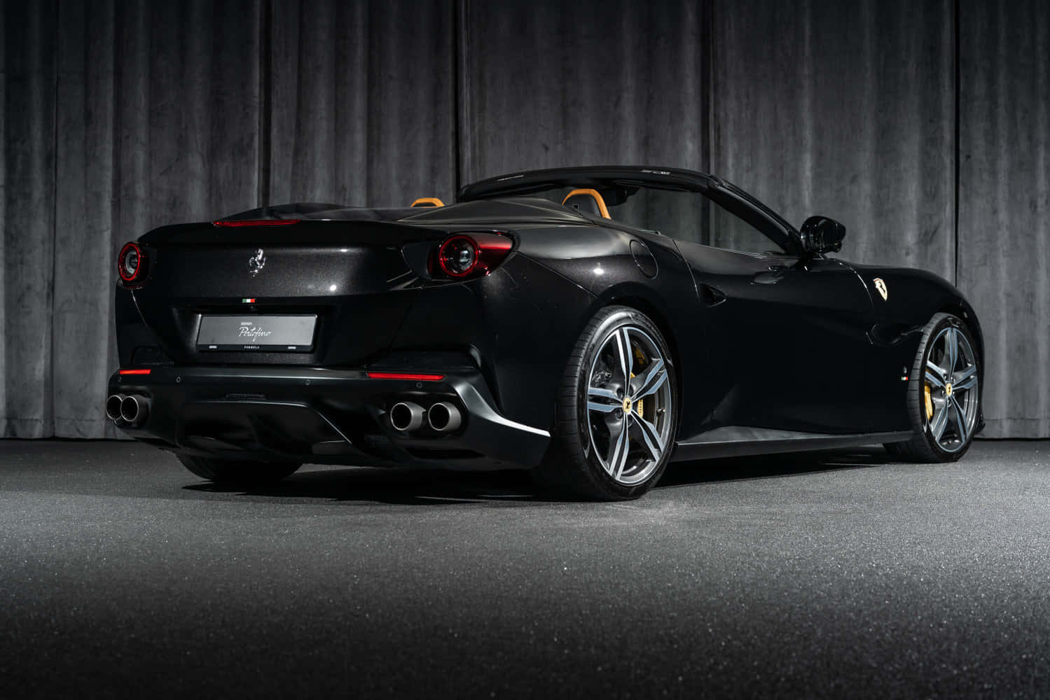 Ferrari Portofino 桌布 壁紙 — 一輛時尚的黑色法拉利 Portofino 敞篷車帶有黃色點綴，在昏暗的攝影棚中，以紋理灰色背景展示。
