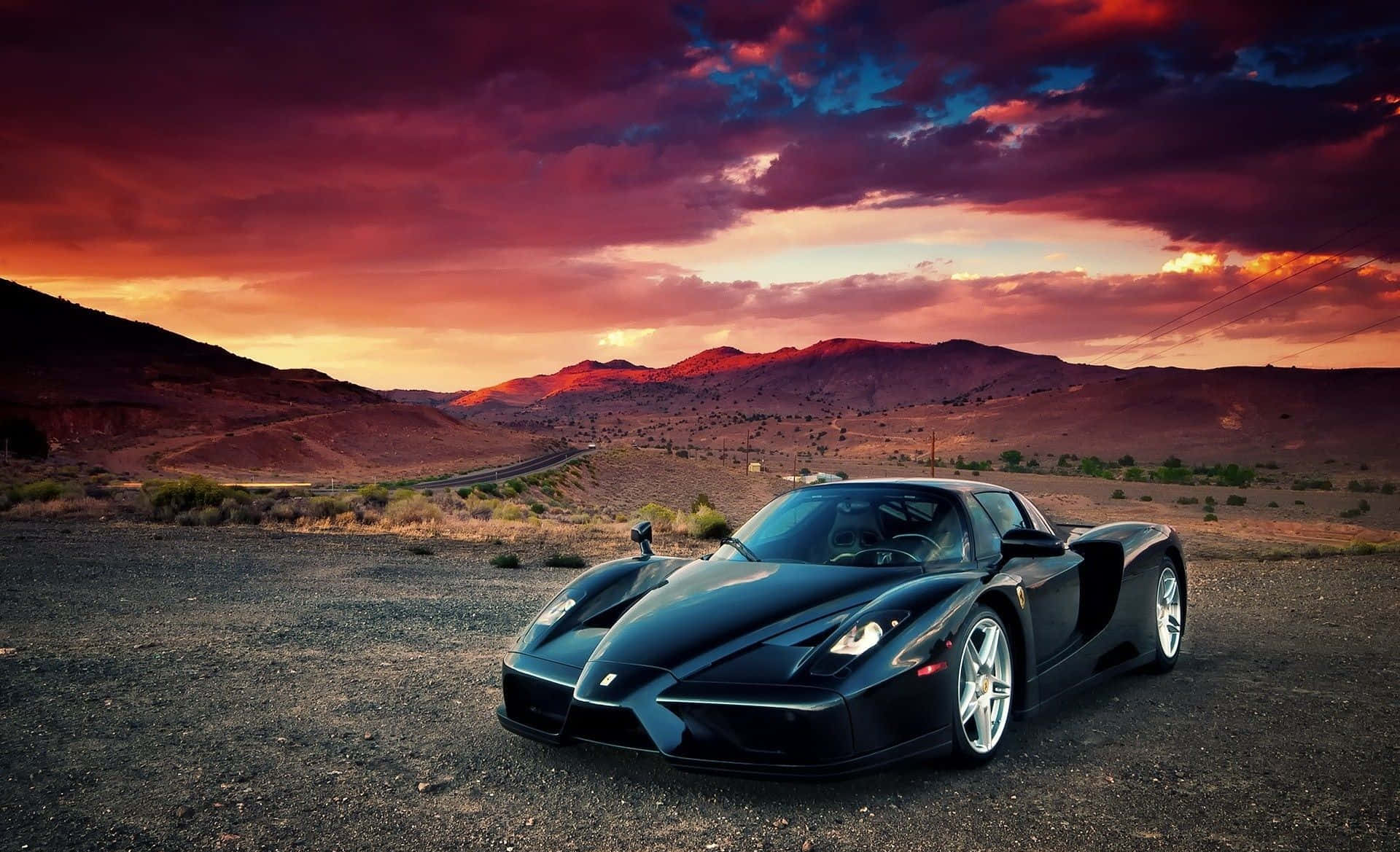 Ferrari Enzo 桌布 壁紙 — 一輛時尚的黑色法拉利Enzo停泊在碎石上，背景是戲劇性的日落天空，有火燒雲和遠山。
