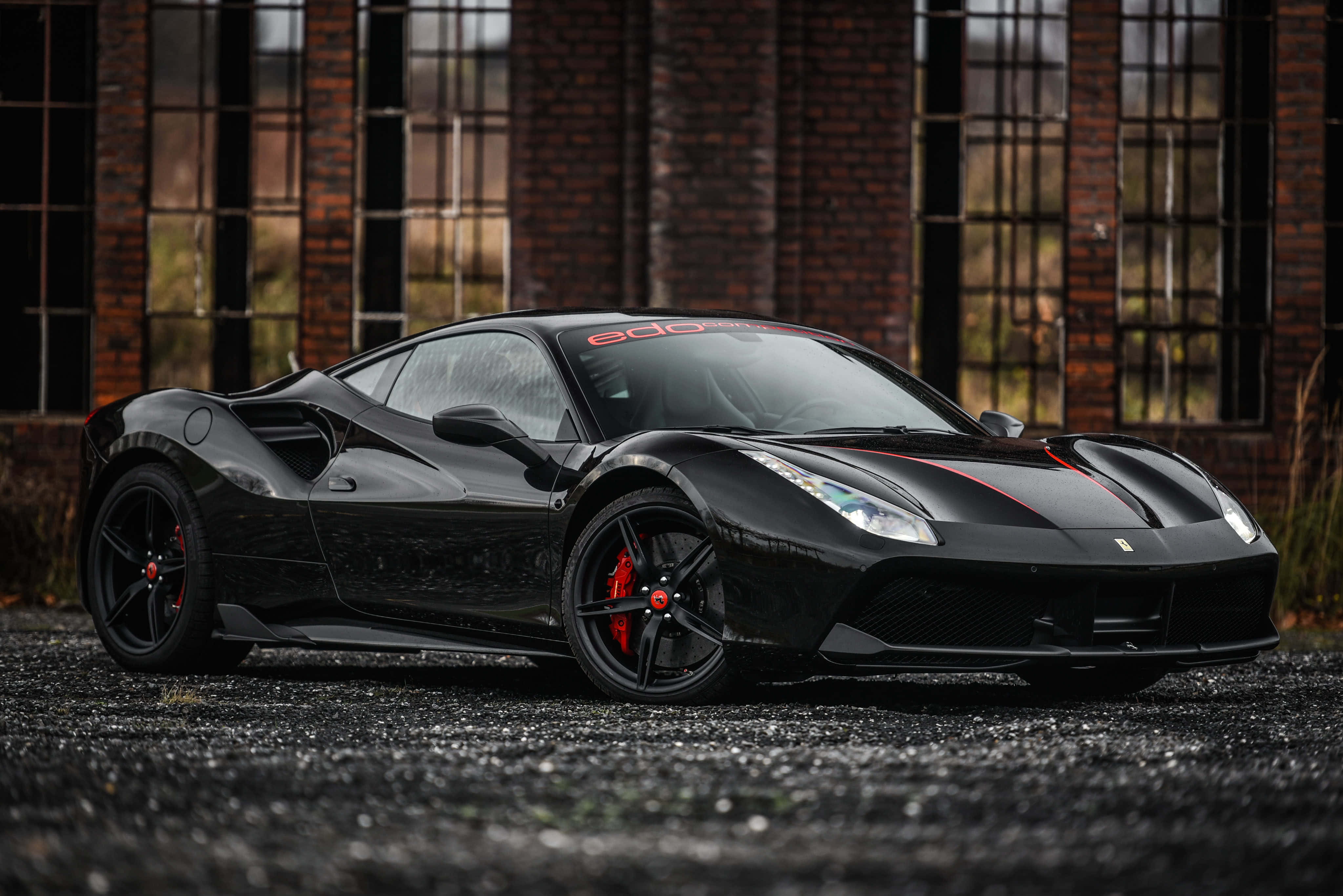 Ferrari 488 Spider 桌布 壁紙 — 一輛時尚的黑色法拉利跑車，帶有紅色點綴，停在碎石路上，前面是磚砌建築，有高窗。
