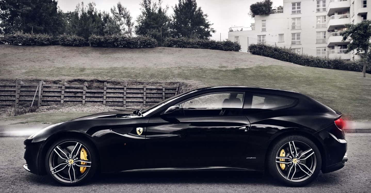 Ferrari Ff 桌布 壁紙 — 一輛時尚的黑色法拉利跑車，帶有黃色制動卡鉗，停放在一條街道上，旁邊是草地山坡和公寓樓。