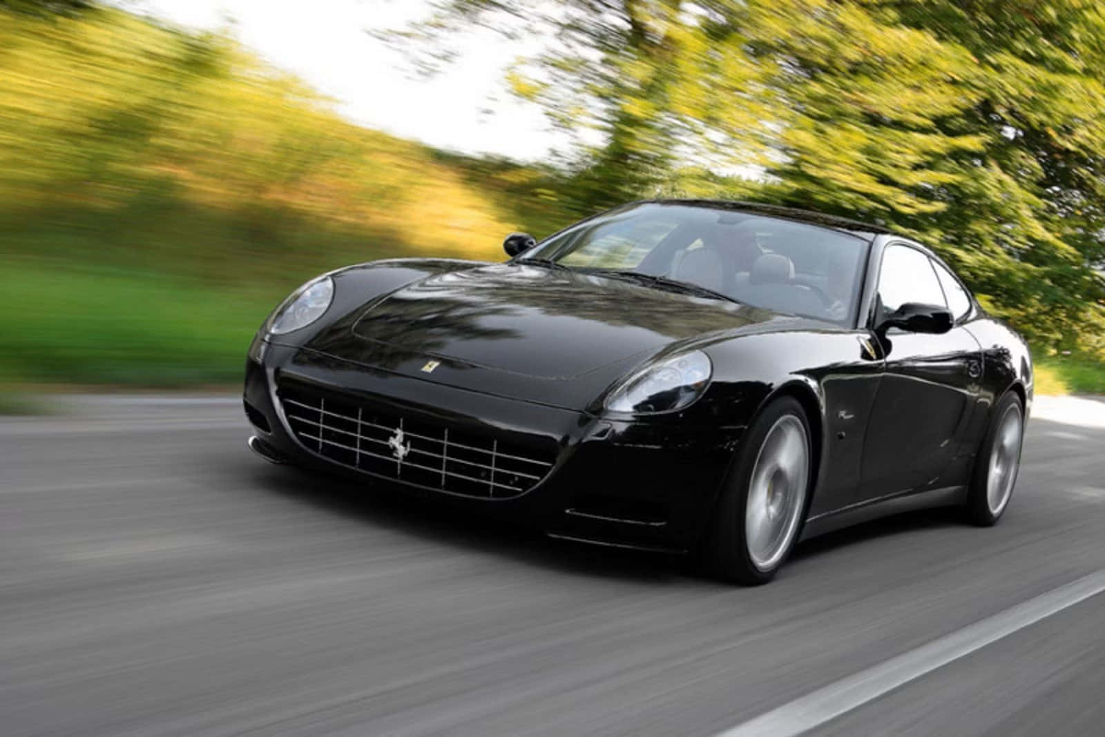 Ferrari 612 Scaglietti 桌布 壁紙 — 一輛時尚的黑色法拉利跑車在樹木成行的道路上飛馳，動態模糊傳達出高速感。