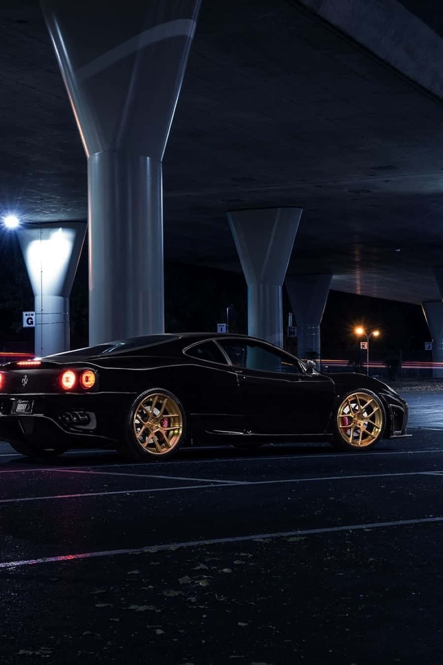Ferrari 360 Modena 桌布 壁紙 — 一輛時尚的黑色法拉利配金色輪圈，夜晚停在混凝土天橋下，尾燈閃爍。
