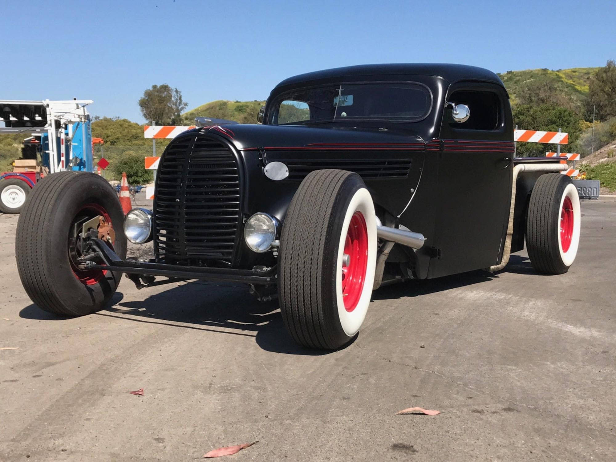old 桌布 壁紙 — 一輛時尚的黑色熱棒卡車，配有紅色車輪和白色側壁輪胎，停在瀝青路面上，天空湛藍。
