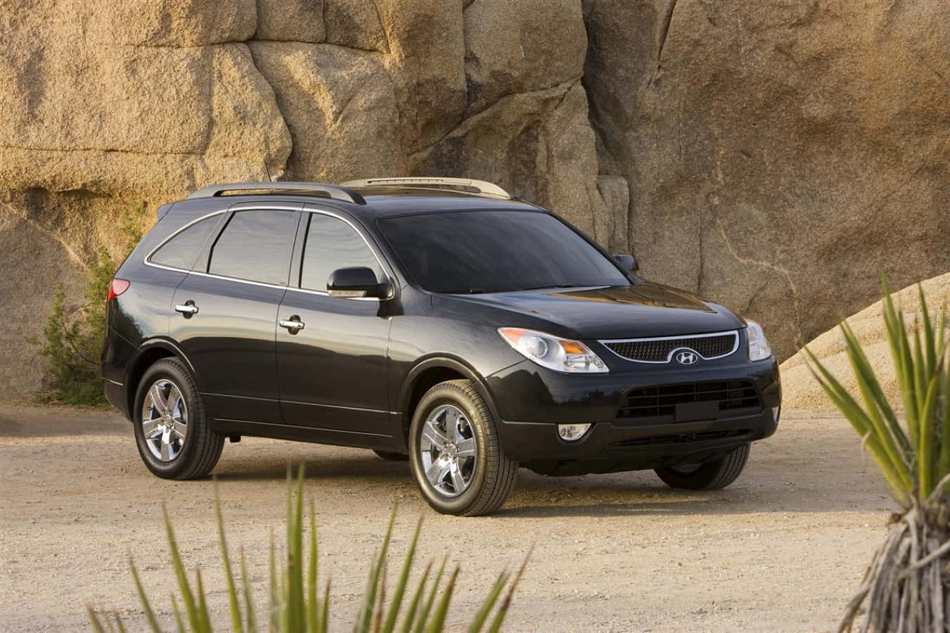 Hyundai Veracruz 桌布 壁紙 — 一輛時尚的黑色現代SUV停泊在沙地上，前方是崎嶇的岩石形成，前景有沙漠植物。