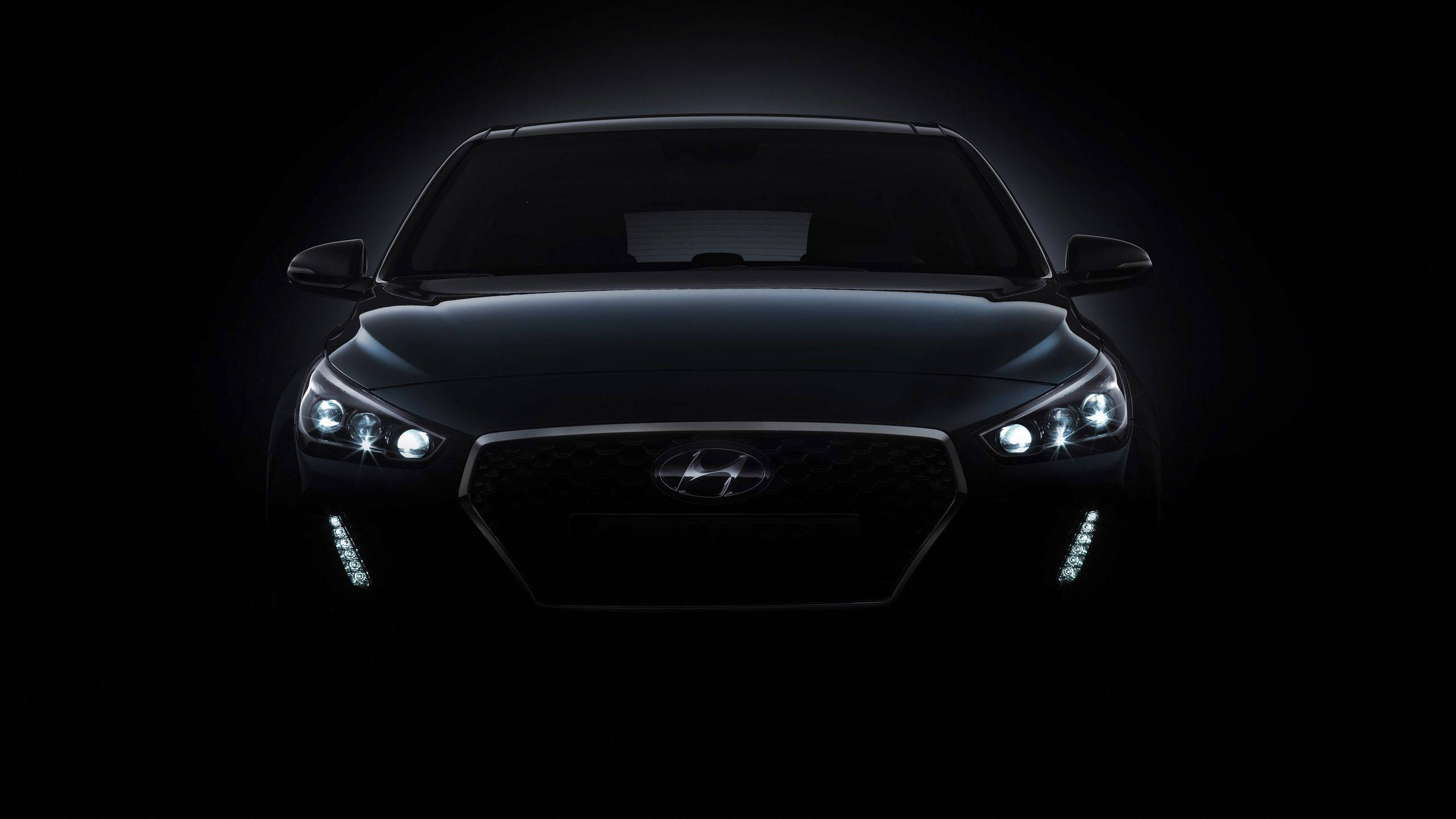 Hyundai 桌布 壁紙 — 一輛時尚的黑色現代汽車在漆黑的攝影棚背景下閃爍著銳利的車頭燈。