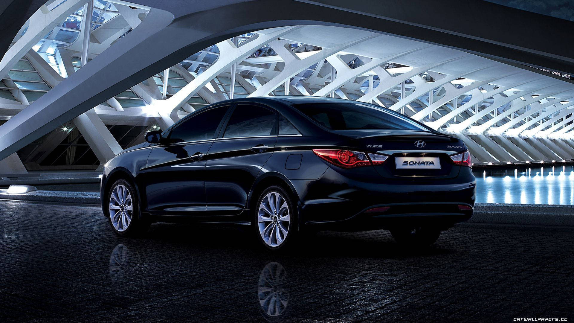 Hyundai 桌布 壁紙 — 一輛時尚的黑色現代索納塔轎車在未來主義白色橋樑結構下的現代建築燈光中閃閃發光。