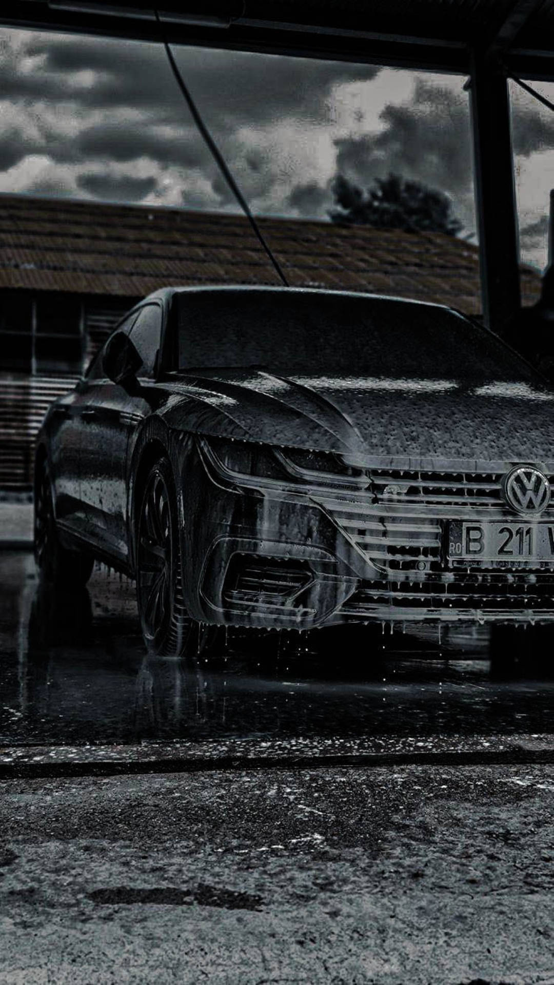 Wash 桌布 壁紙 — 一輛時尚的黑色福斯偉根轎車在昏暗的洗車場中，在雨滴下閃閃發光，頭頂有暴風雲。