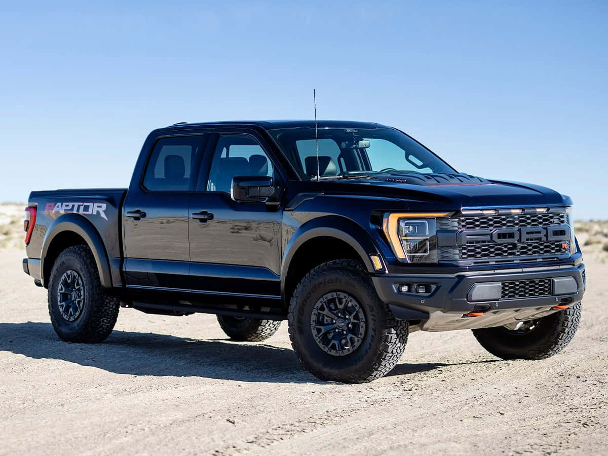 福特 桌布 壁紙 — 一輛時尚的黑色福特 F-150 Raptor 皮卡車，在晴朗的藍天下，停放在陽光明媚的沙漠碎石路上。